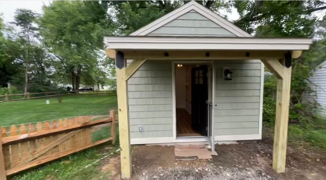 A small house with a porch and a fence in the backyard.