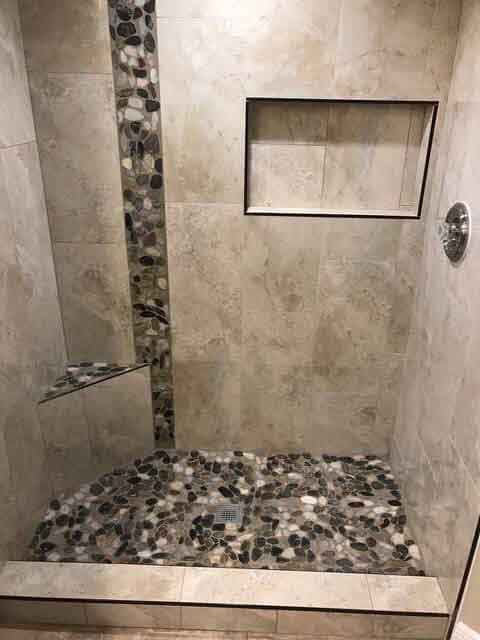 A walk in shower with a tiled floor and a glass door.