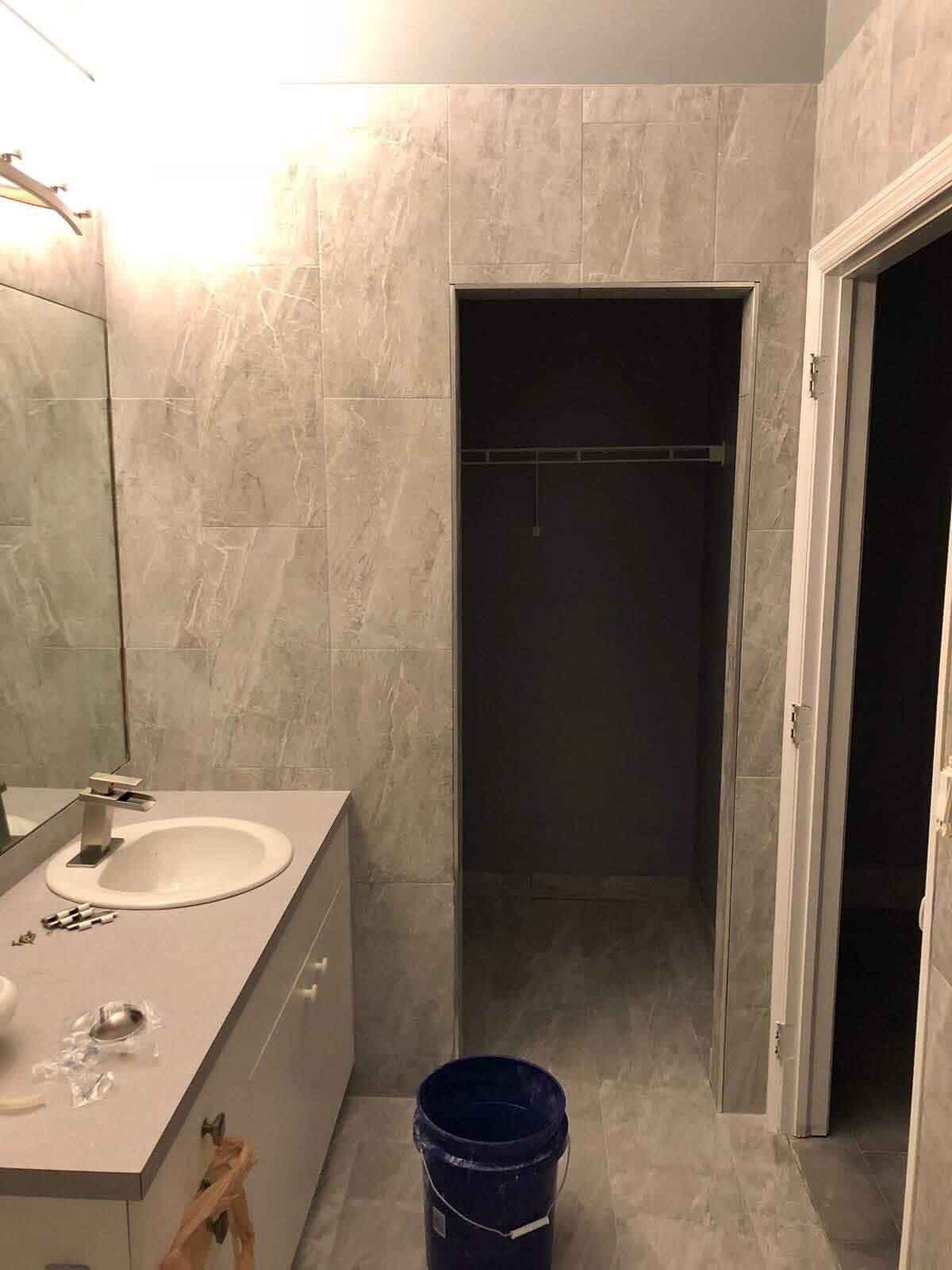 A bathroom with a sink , mirror and a blue bucket.