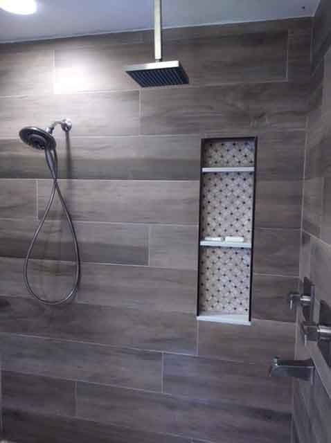 A shower with a built in shelf and a shower head.