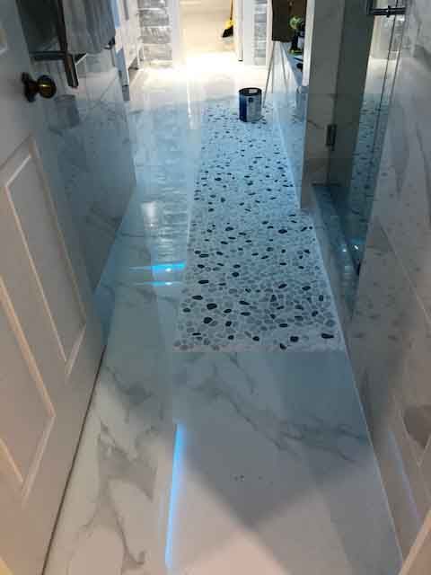 A hallway in a bathroom with white tiles and a rug on the floor.