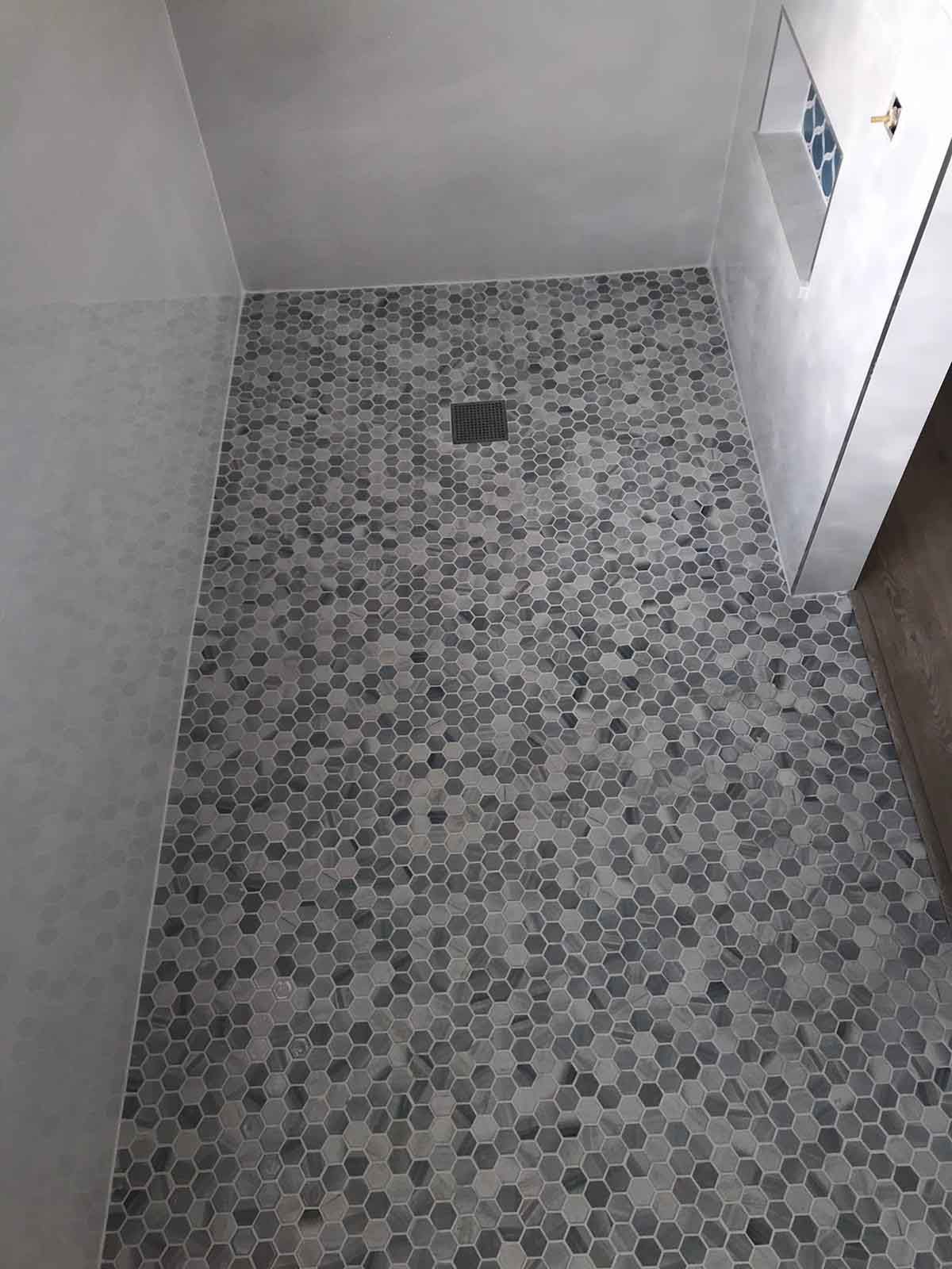 A shower stall with a tiled floor and a drain.