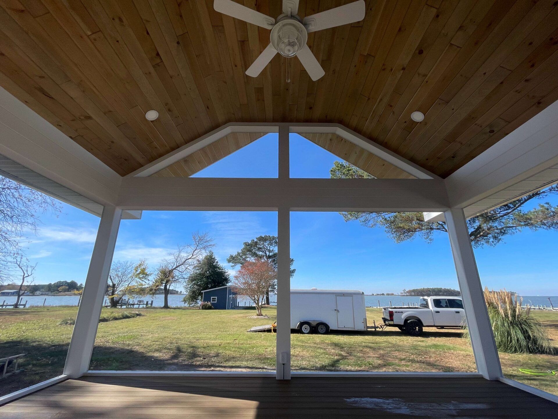 A screened in porch with a ceiling fan and a view of a lake.