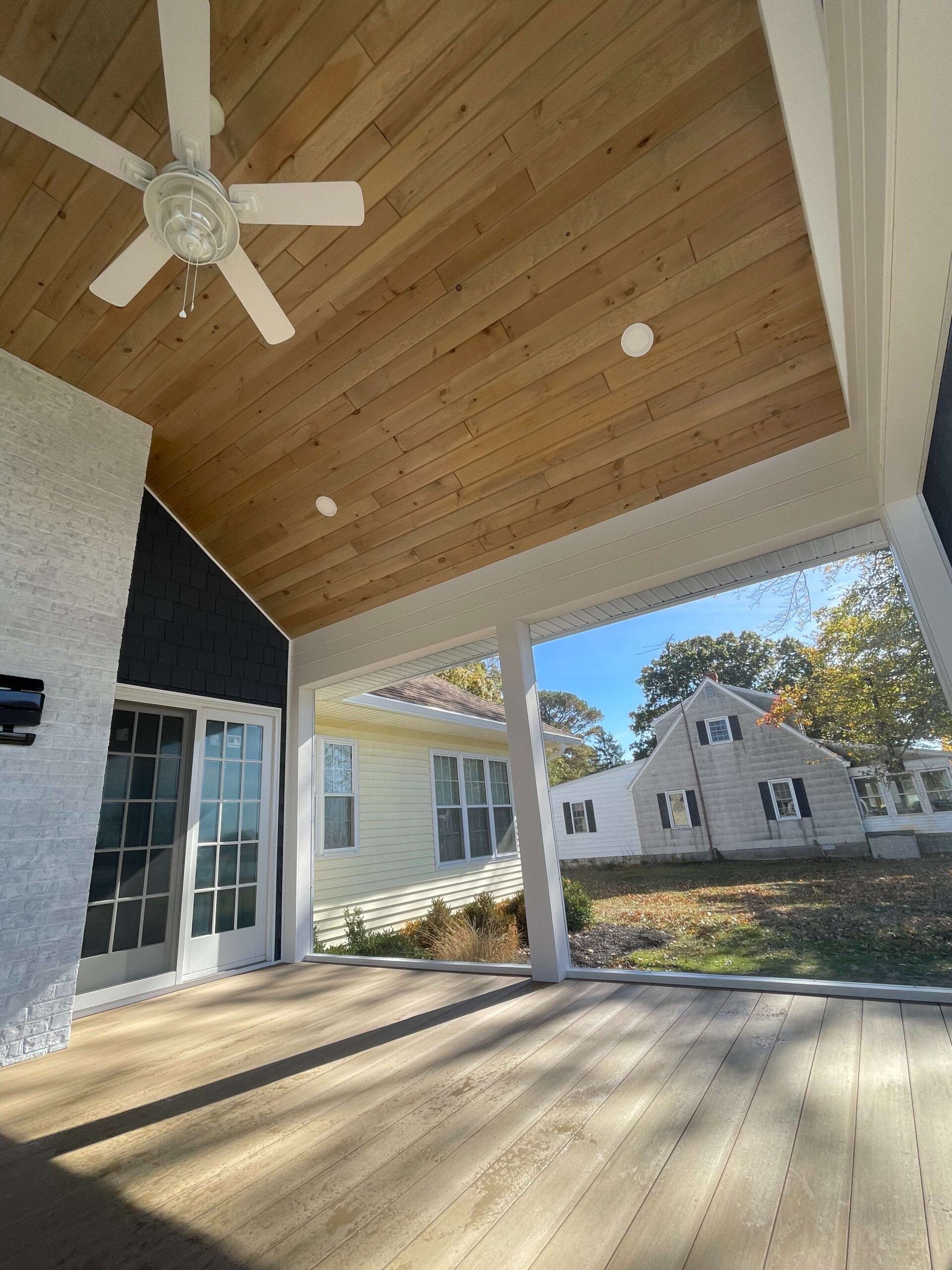 A porch with a wooden ceiling and a ceiling fan.