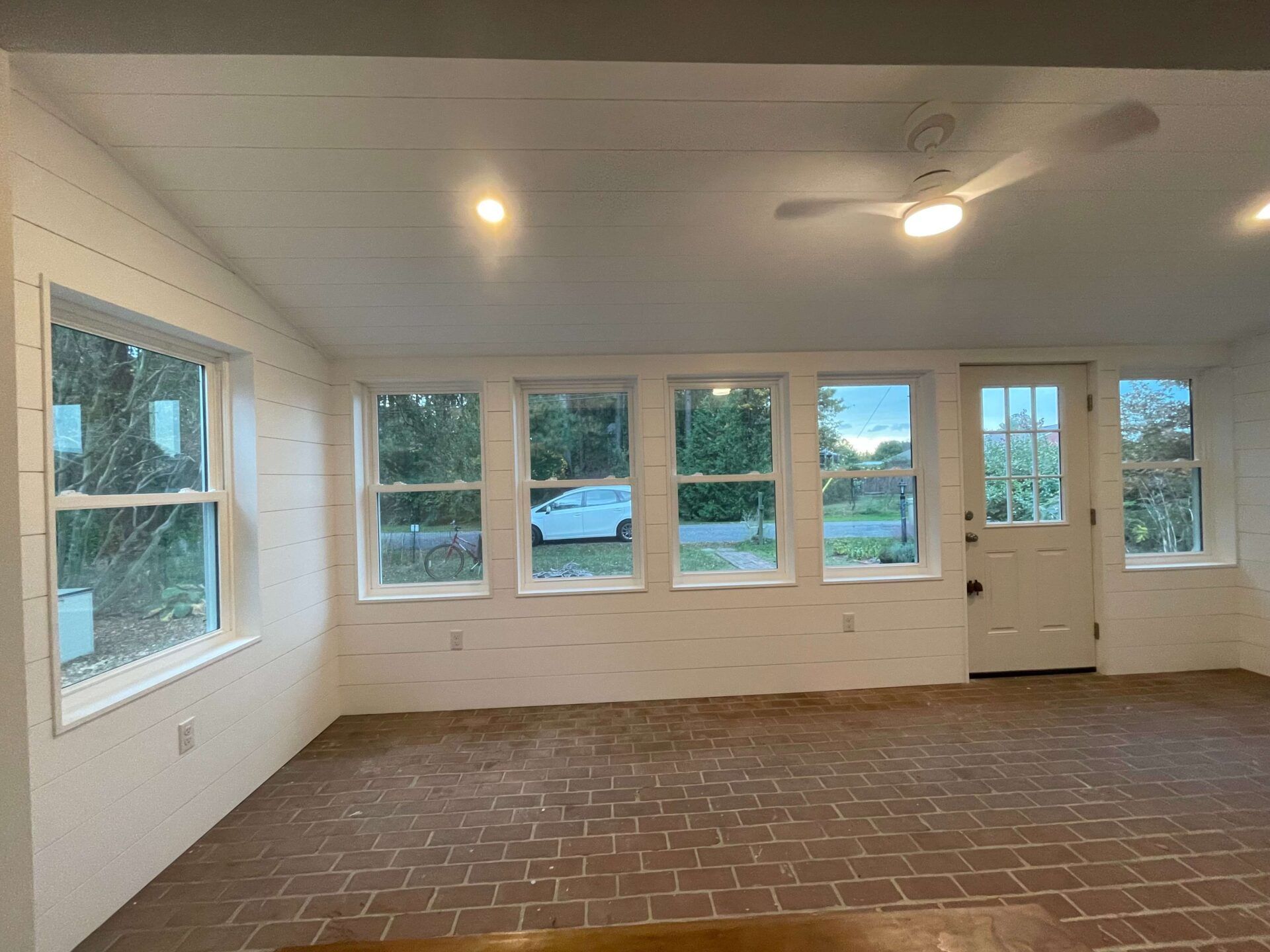 An empty room with a brick floor , white walls , and a ceiling fan.