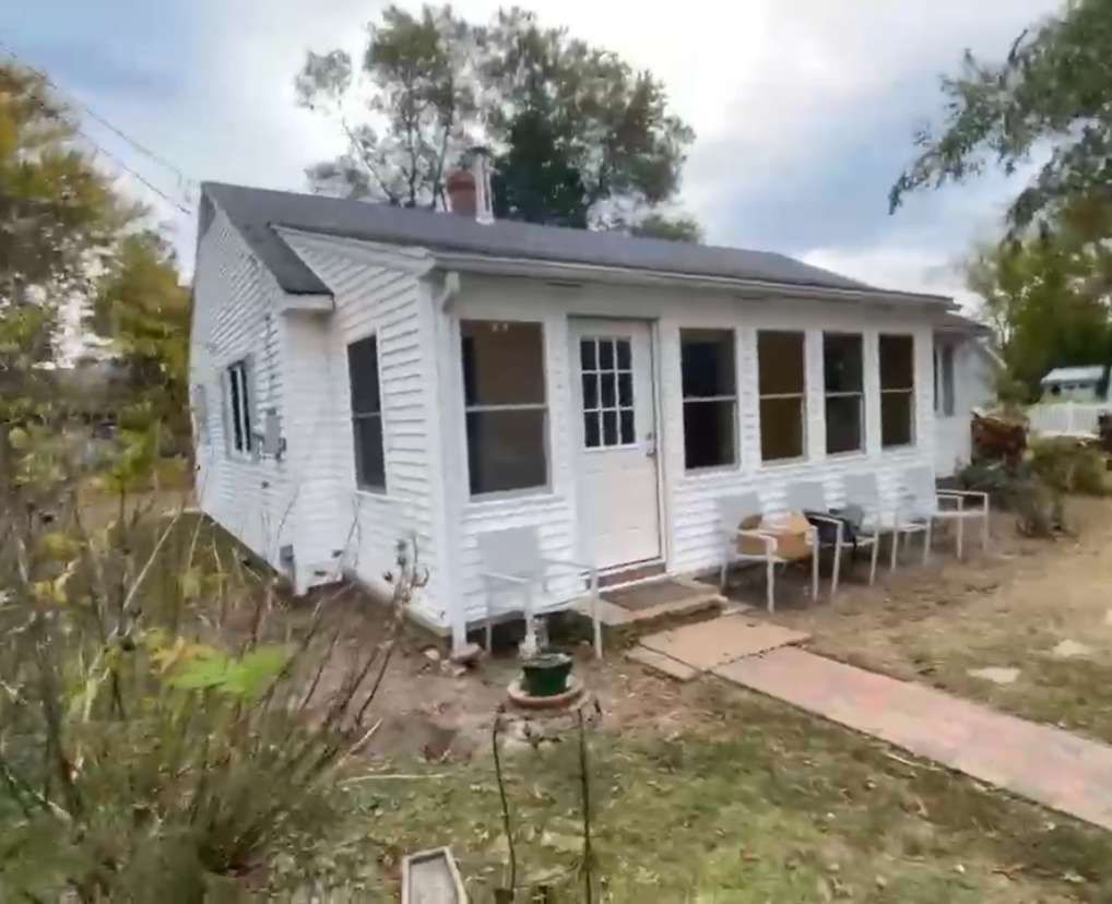 A small white house with a porch and chairs in front of it.