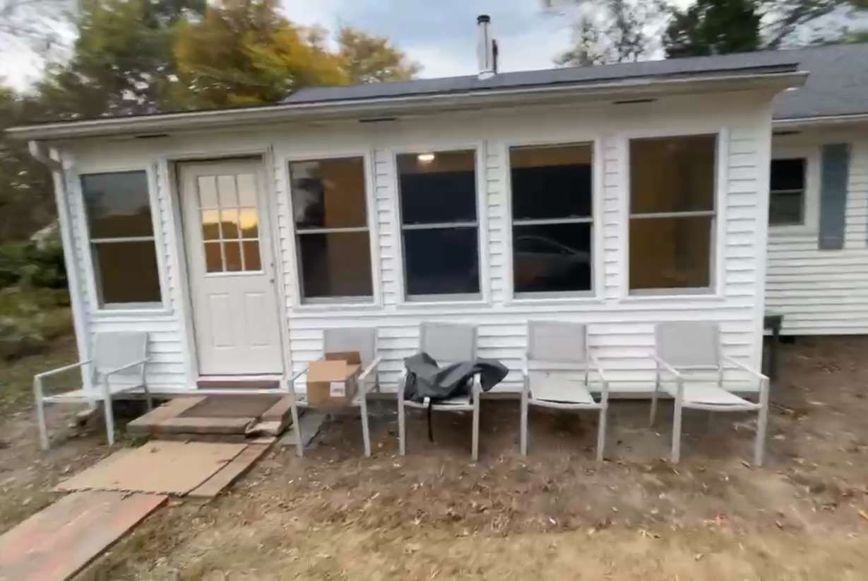 A small white house with a row of chairs in front of it.