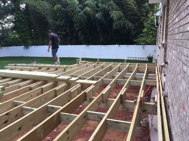 A man is standing on top of a wooden deck under construction.