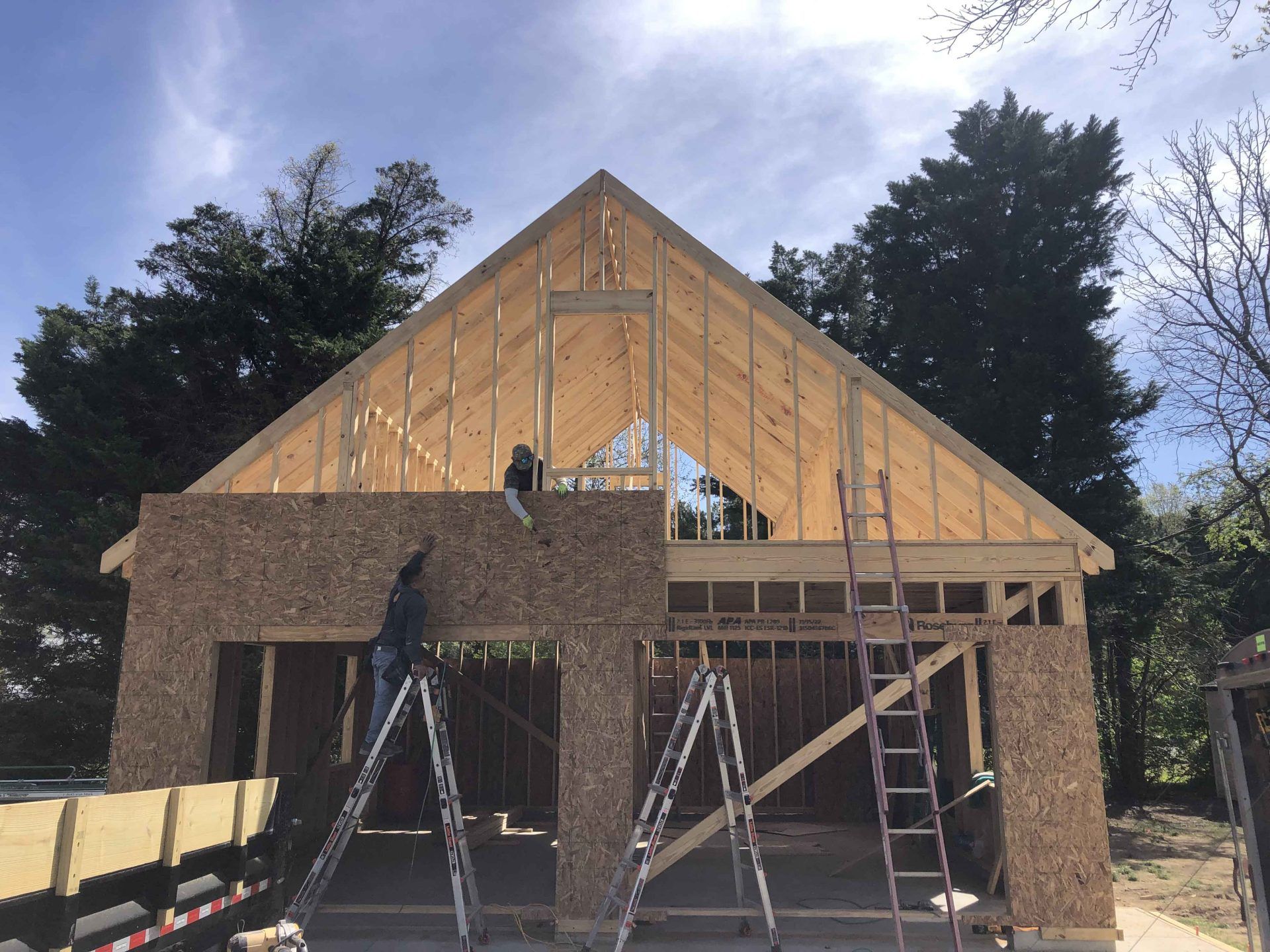 A man is standing on a ladder in front of a house under construction.