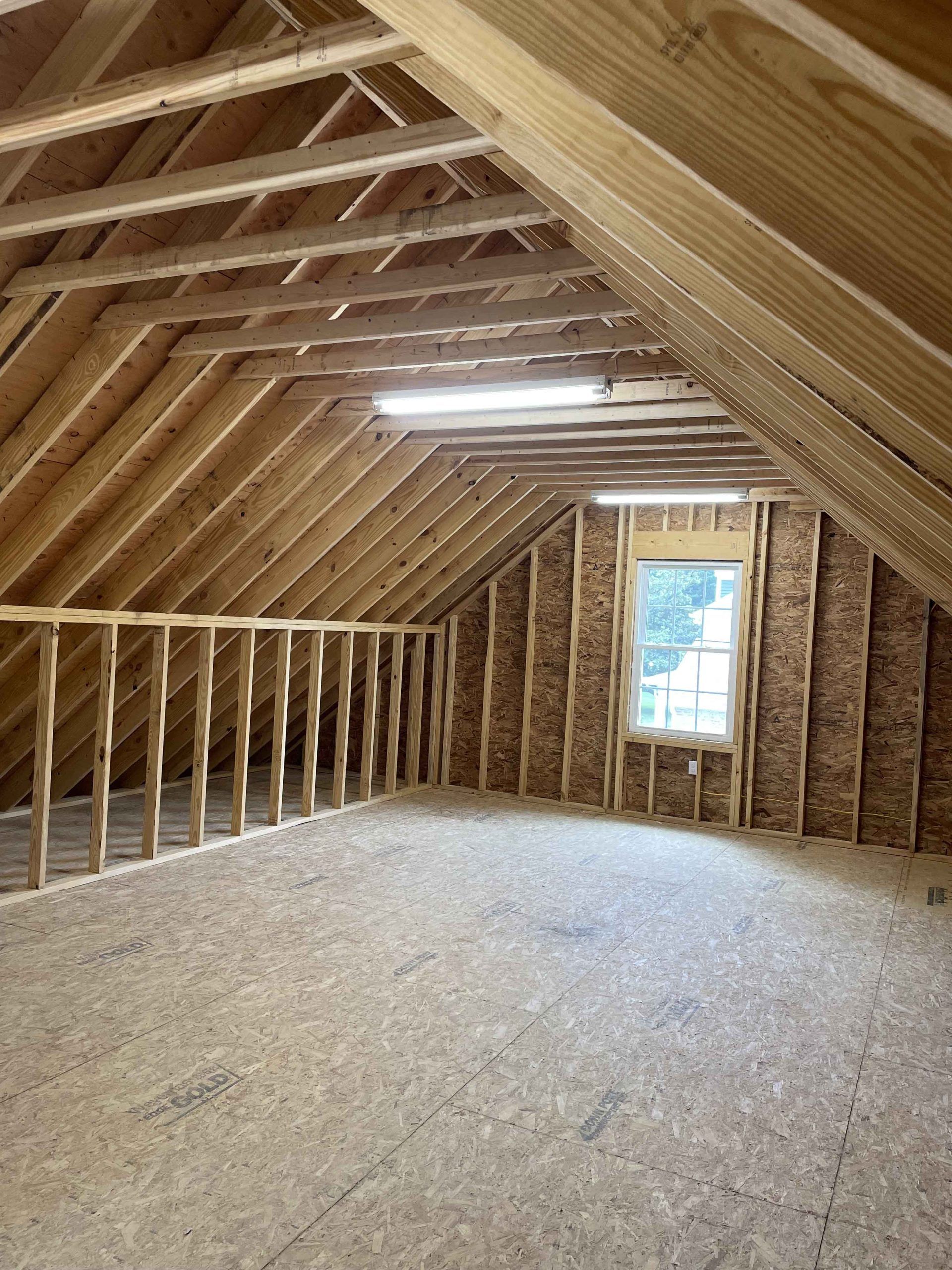 An empty attic with wooden beams and a window.