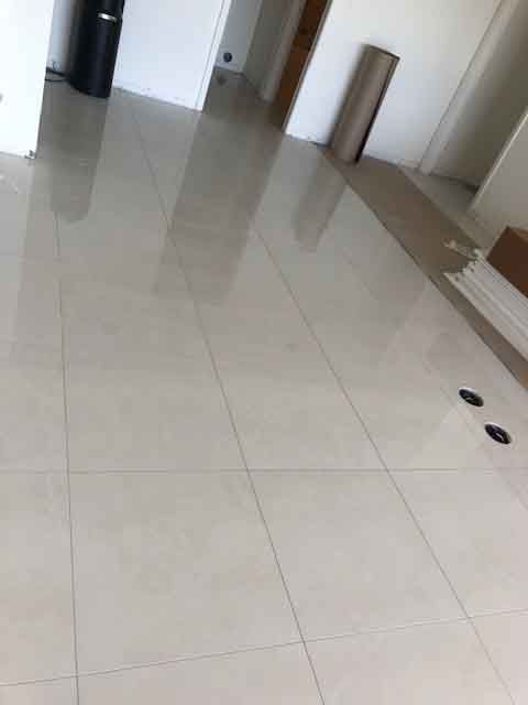 A white tiled floor in a room with a reflection of the floor in the tiles.
