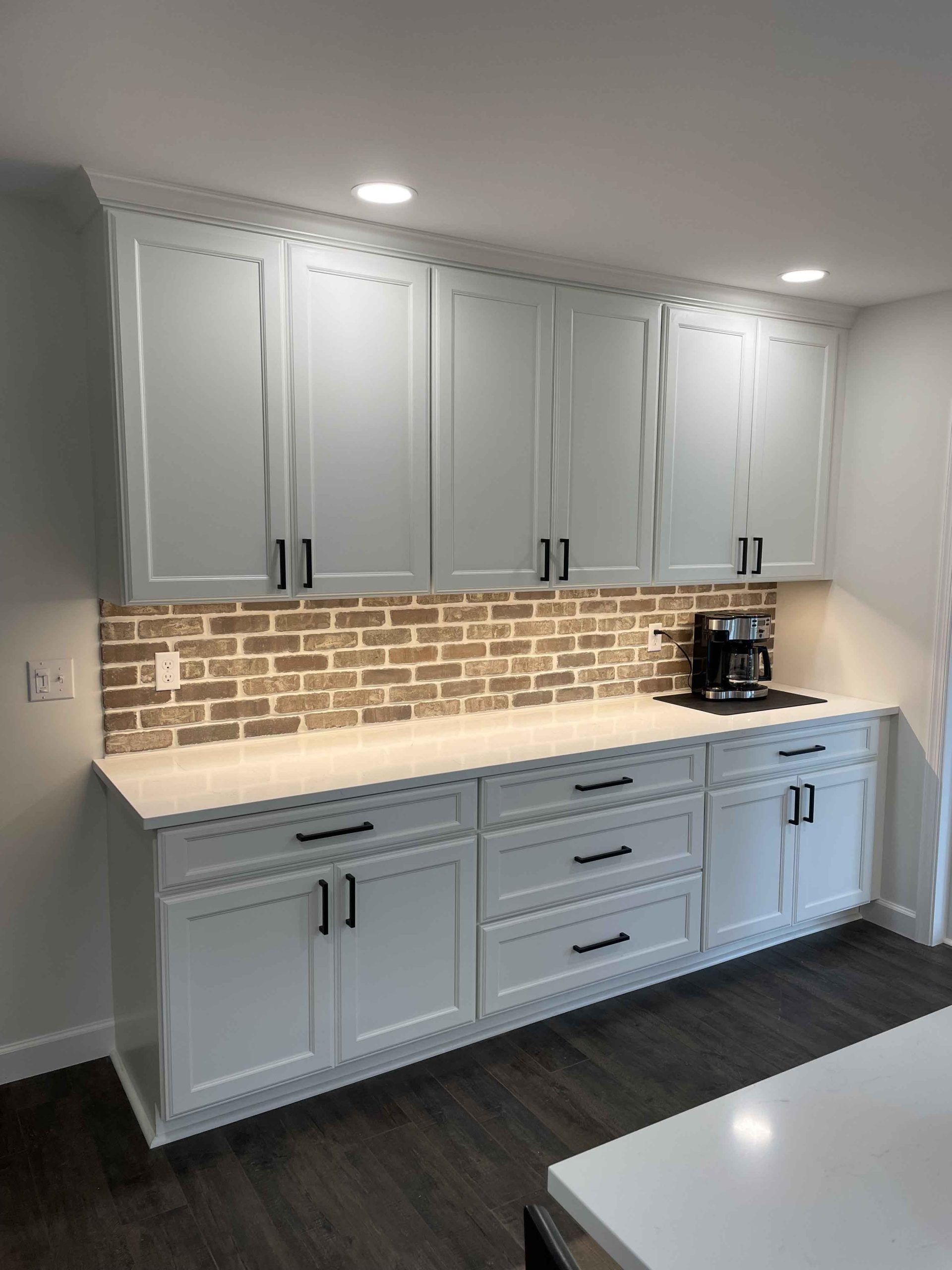 A kitchen with white cabinets and a brick wall.