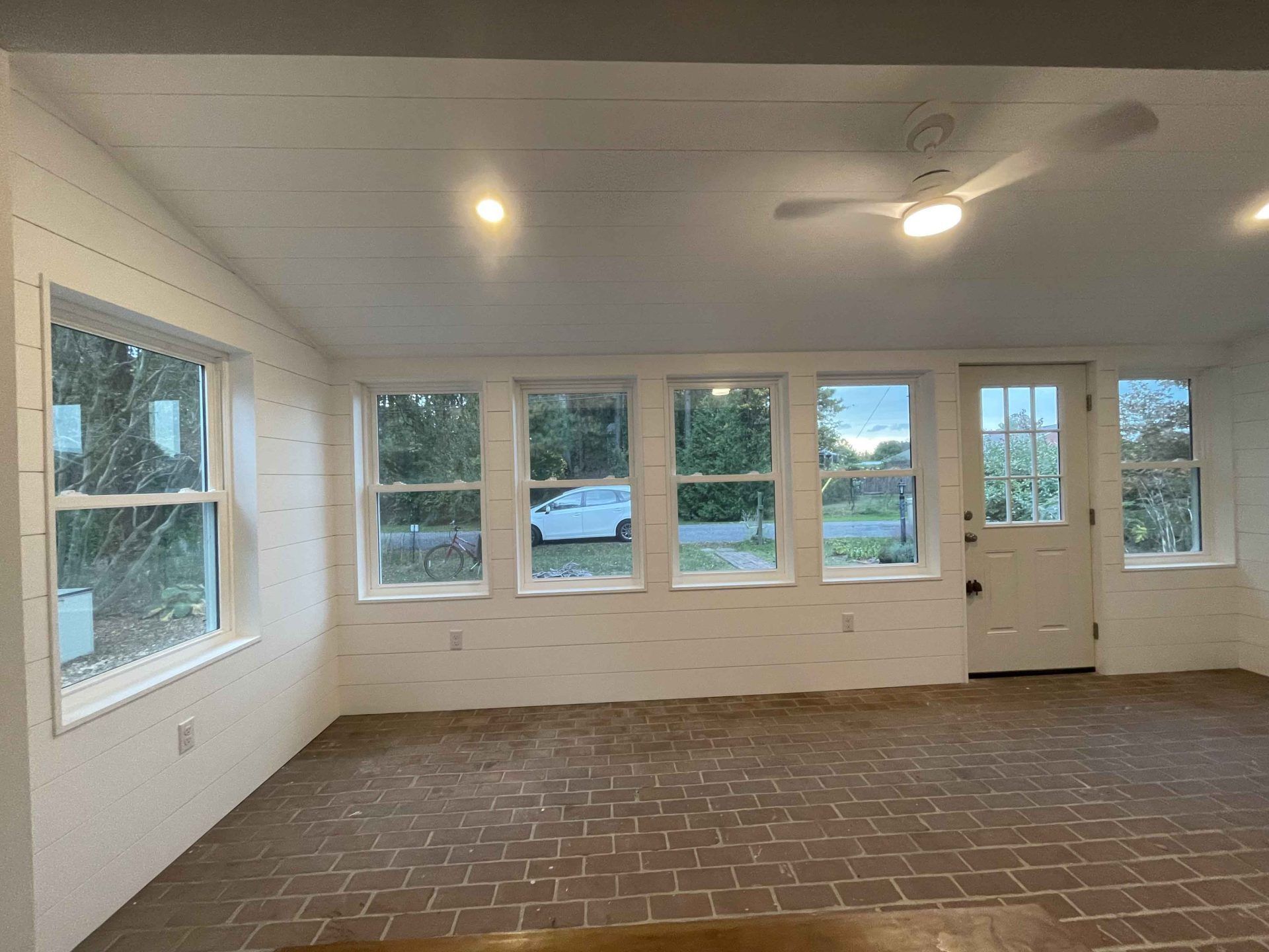 An empty room with a lot of windows and a ceiling fan.
