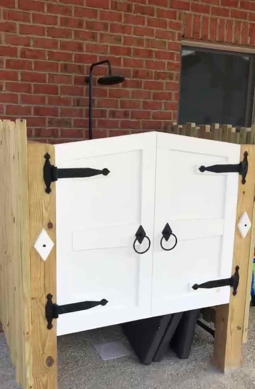 A white cabinet with black hinges is sitting in front of a brick wall.