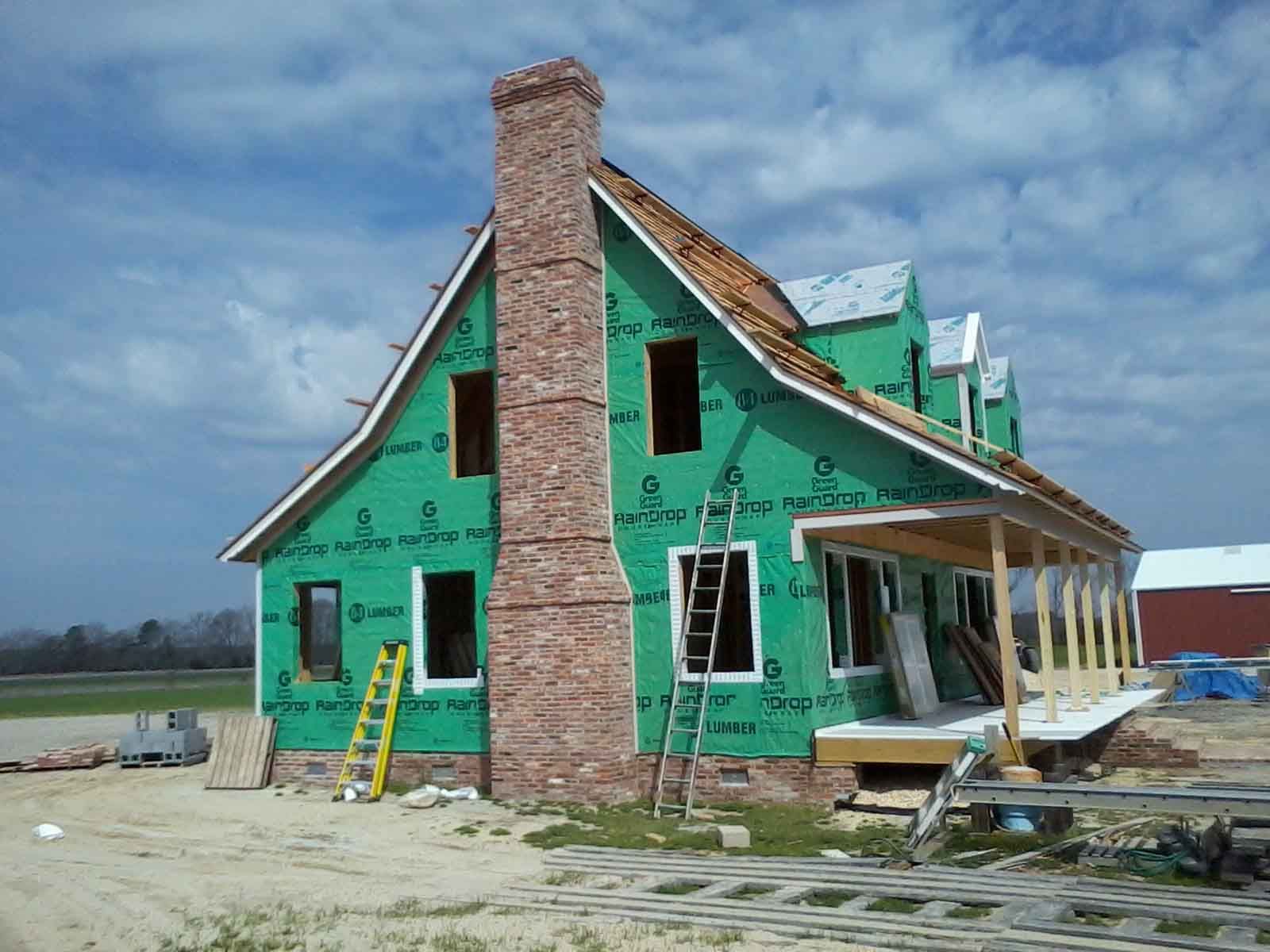 A house under construction with green siding and a brick chimney