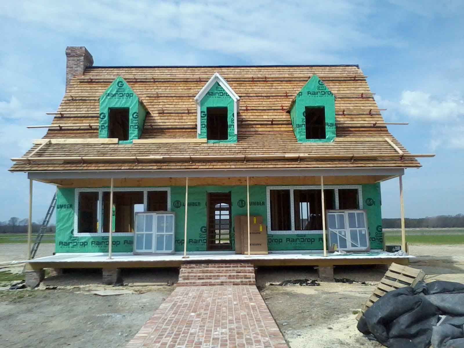 A house under construction with green siding and a brick walkway