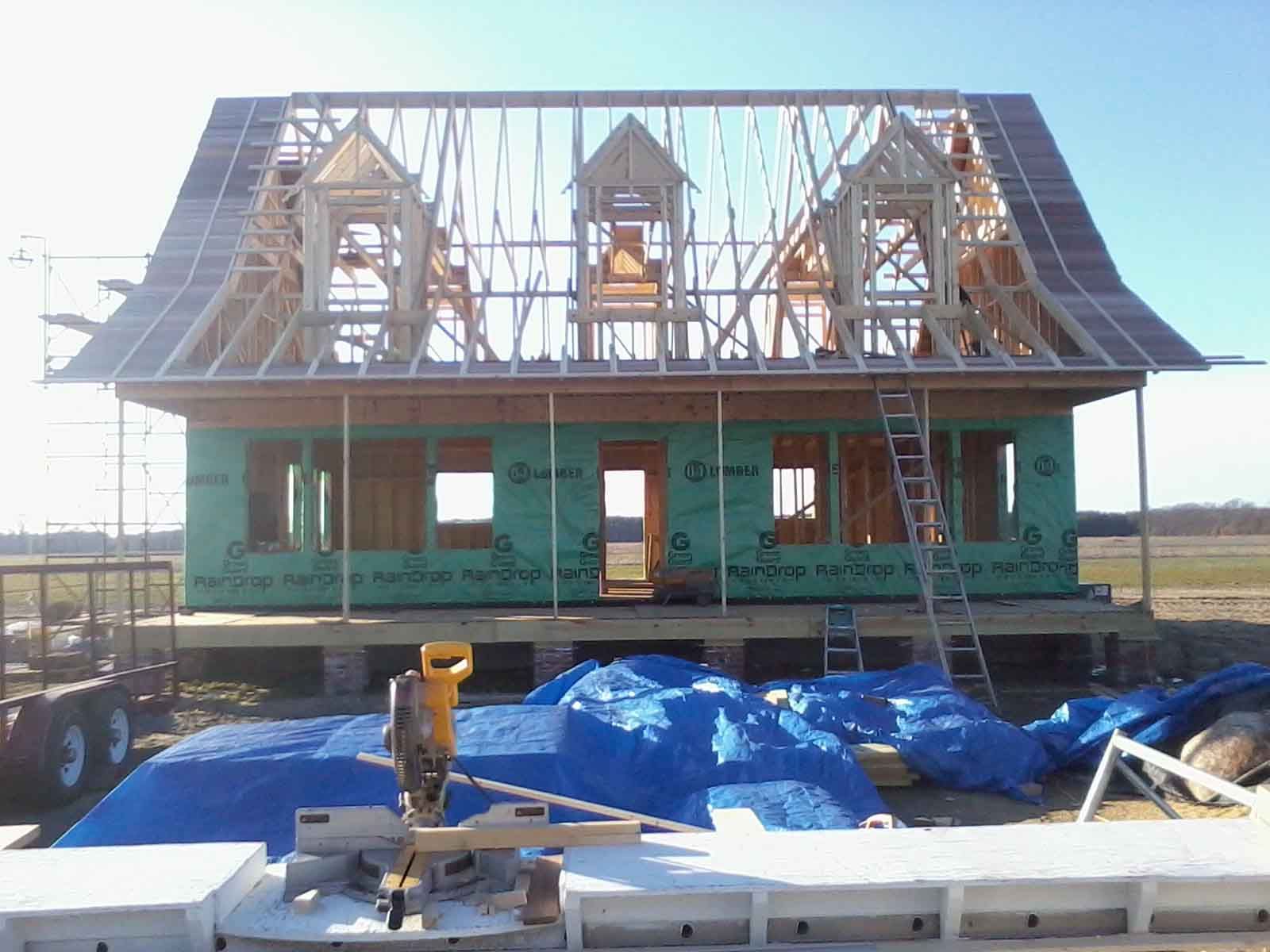 A house is being built in a field with blue tarps on the ground