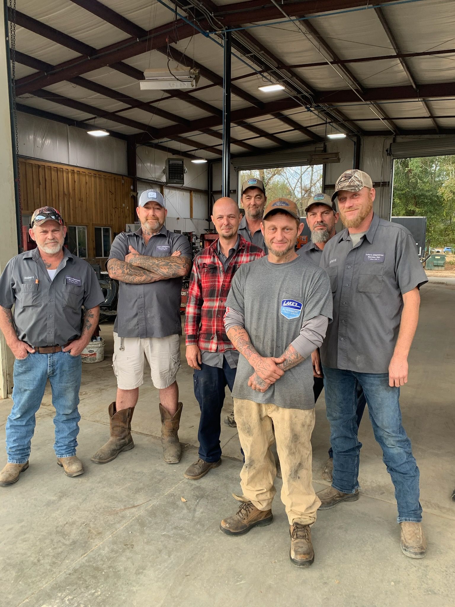 Seven workers in casual workwear stand together in a large, open industrial shop.