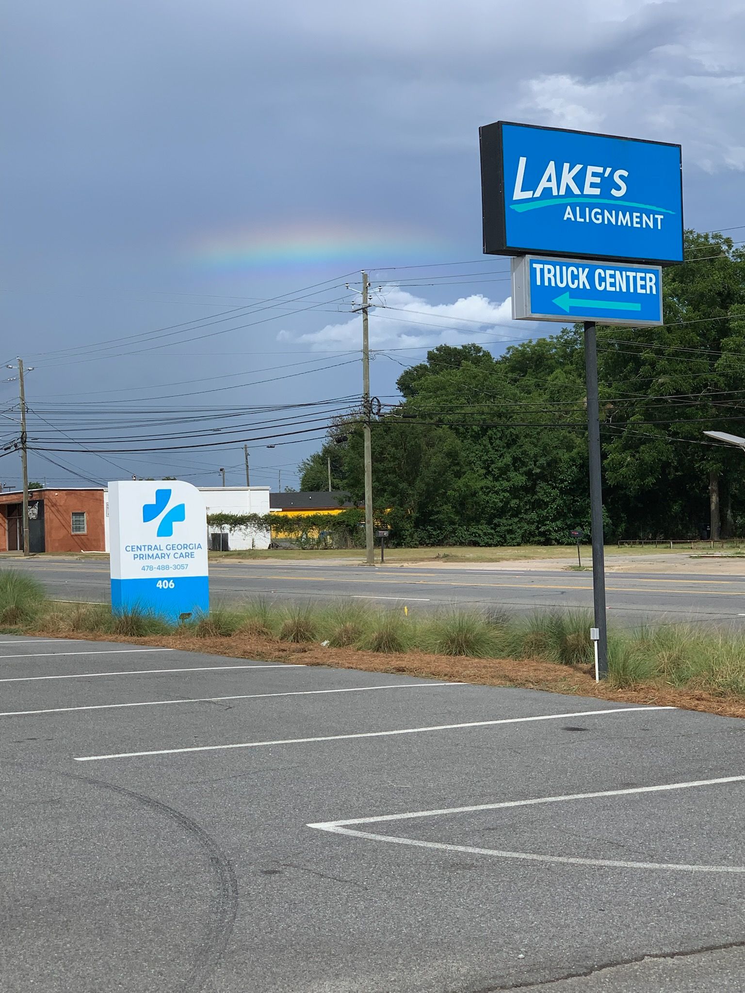 Lake's Auto & Truck Center sign with rainbow and flock of birds against a cloudy sky.