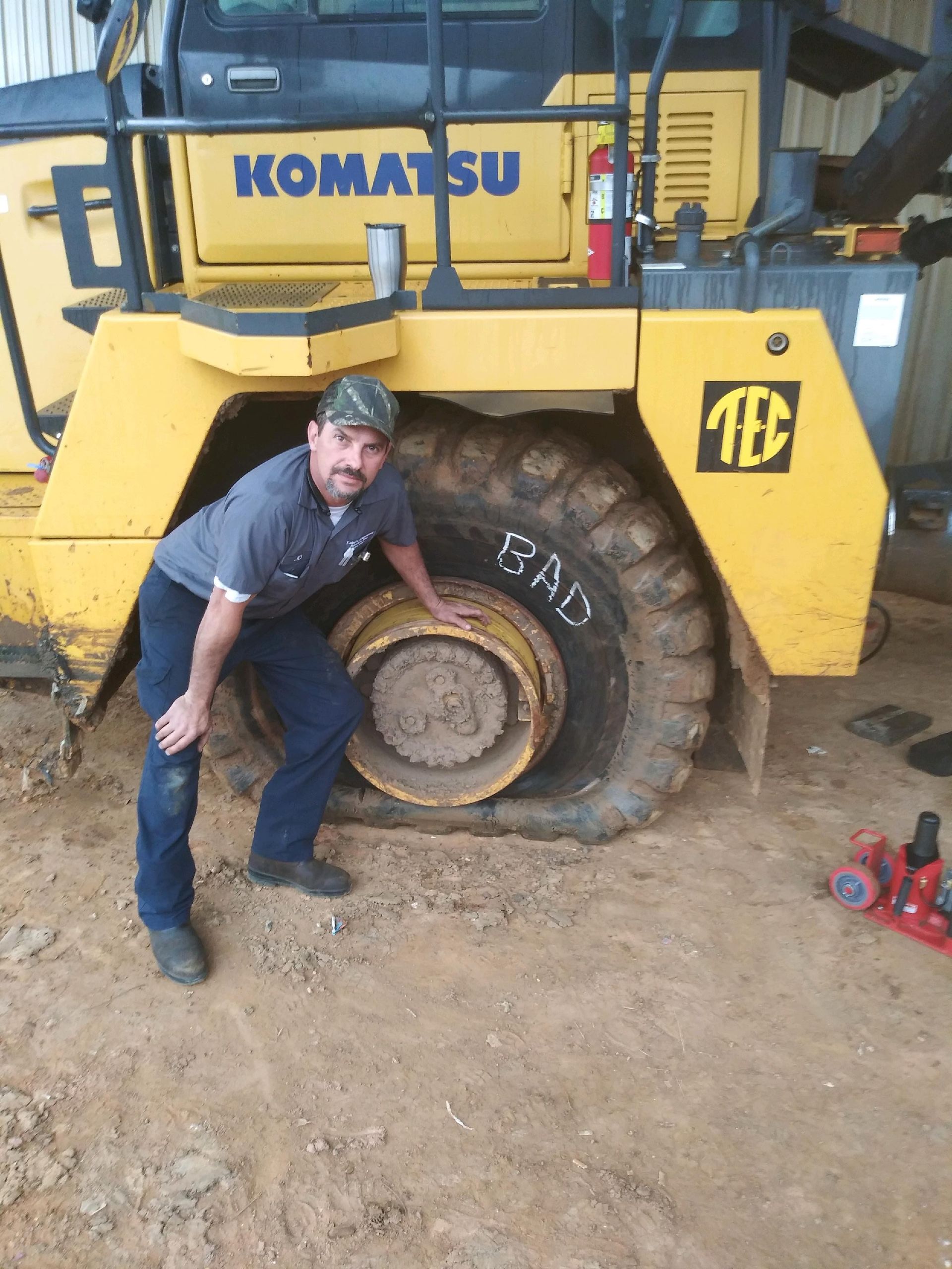 Man inspecting a flat tire on a large yellow Komatsu truck; 