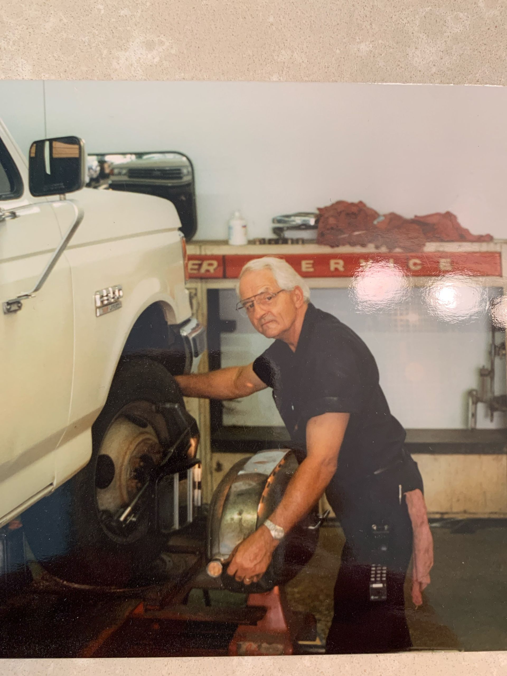 Man working on a car's wheel in a garage, wearing dark uniform.
