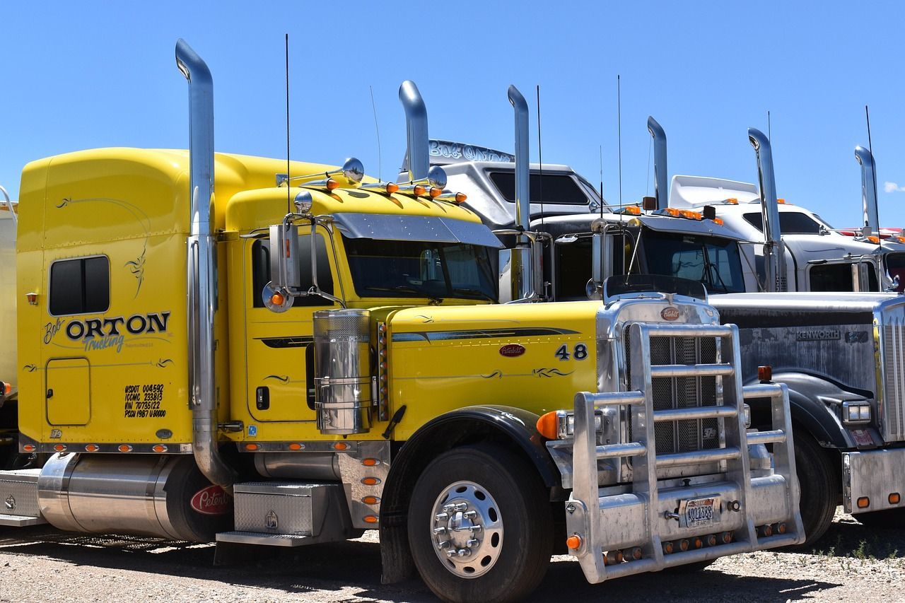 Yellow semi-truck with chrome details, parked outside on a sunny day next to other semi-trucks.