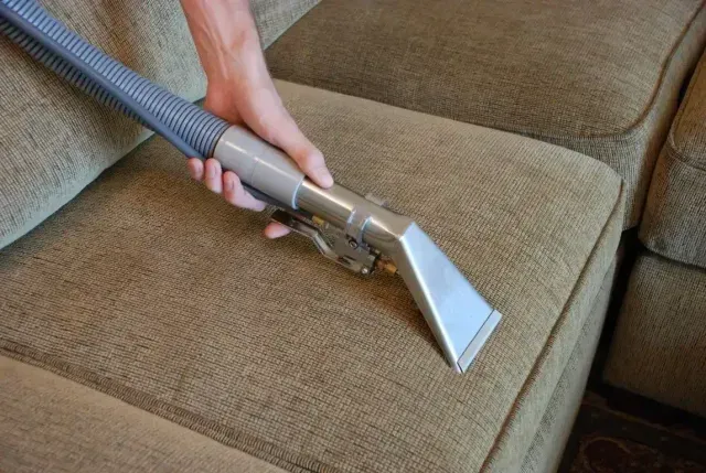 Vacuum cleaner nozzle cleaning a beige sofa cushion