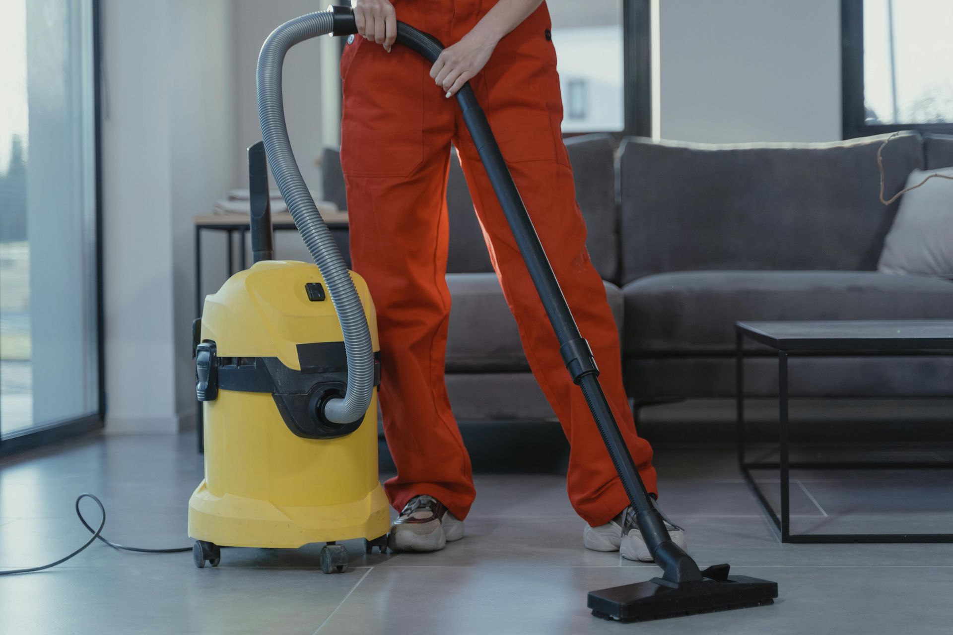 Person vacuuming a living room floor with a yellow canister vacuum and black hose