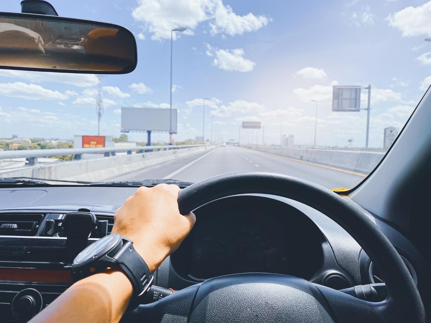 Driver's hand on steering wheel, driving on a sunny highway.