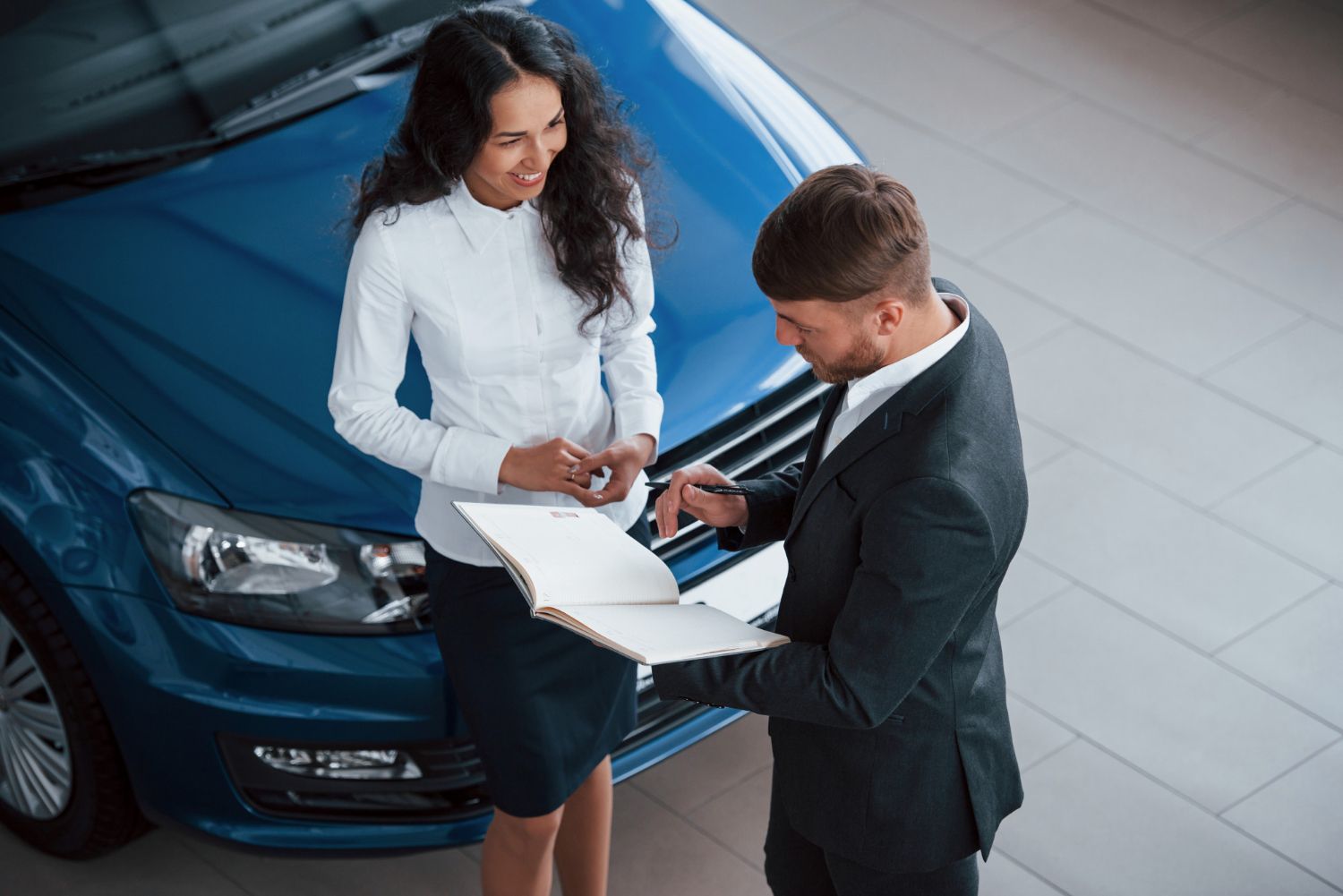 Woman and man looking at paperwork by a blue car in a showroom.