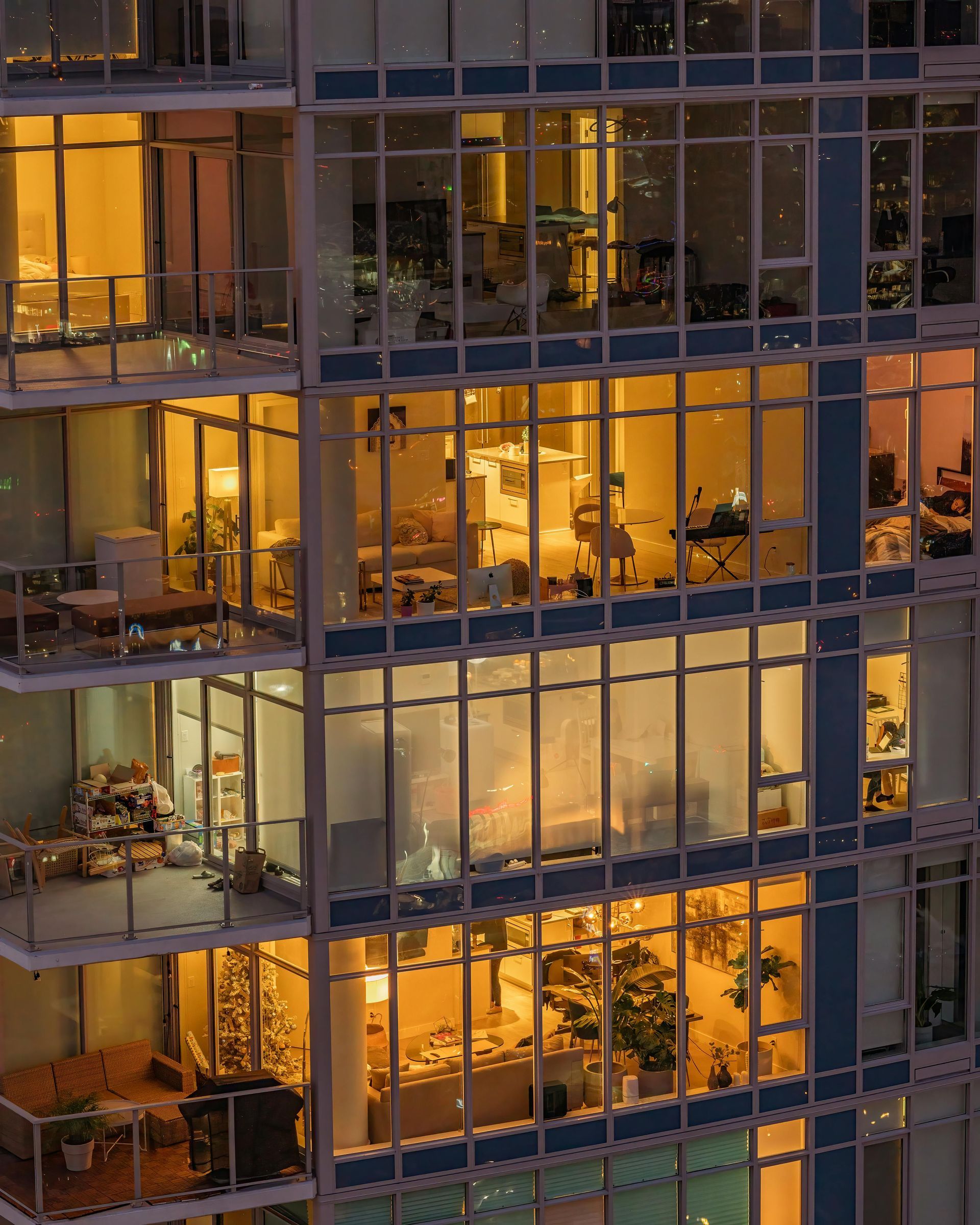 Lit apartment windows in a skyscraper at dusk; warm interior lights contrast with the dark exterior.