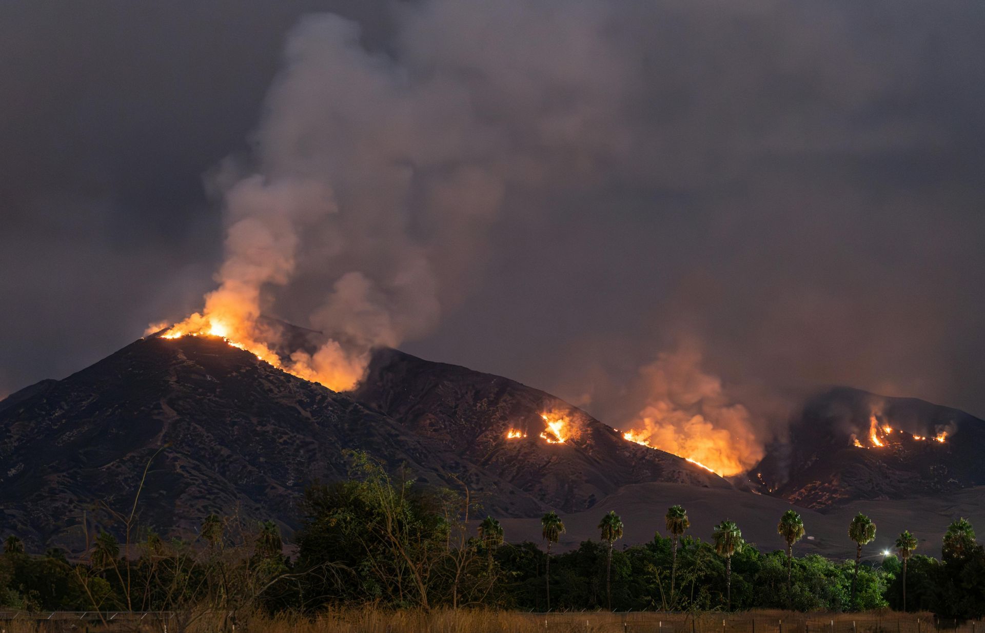 Mountain engulfed in flames at night; smoke billowing into the dark sky.
