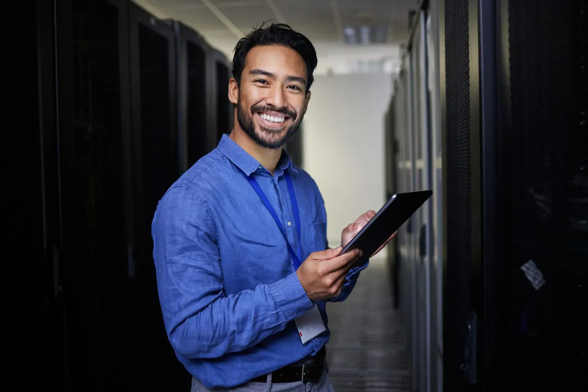 IT professional smiles while holding a tablet in a server room.