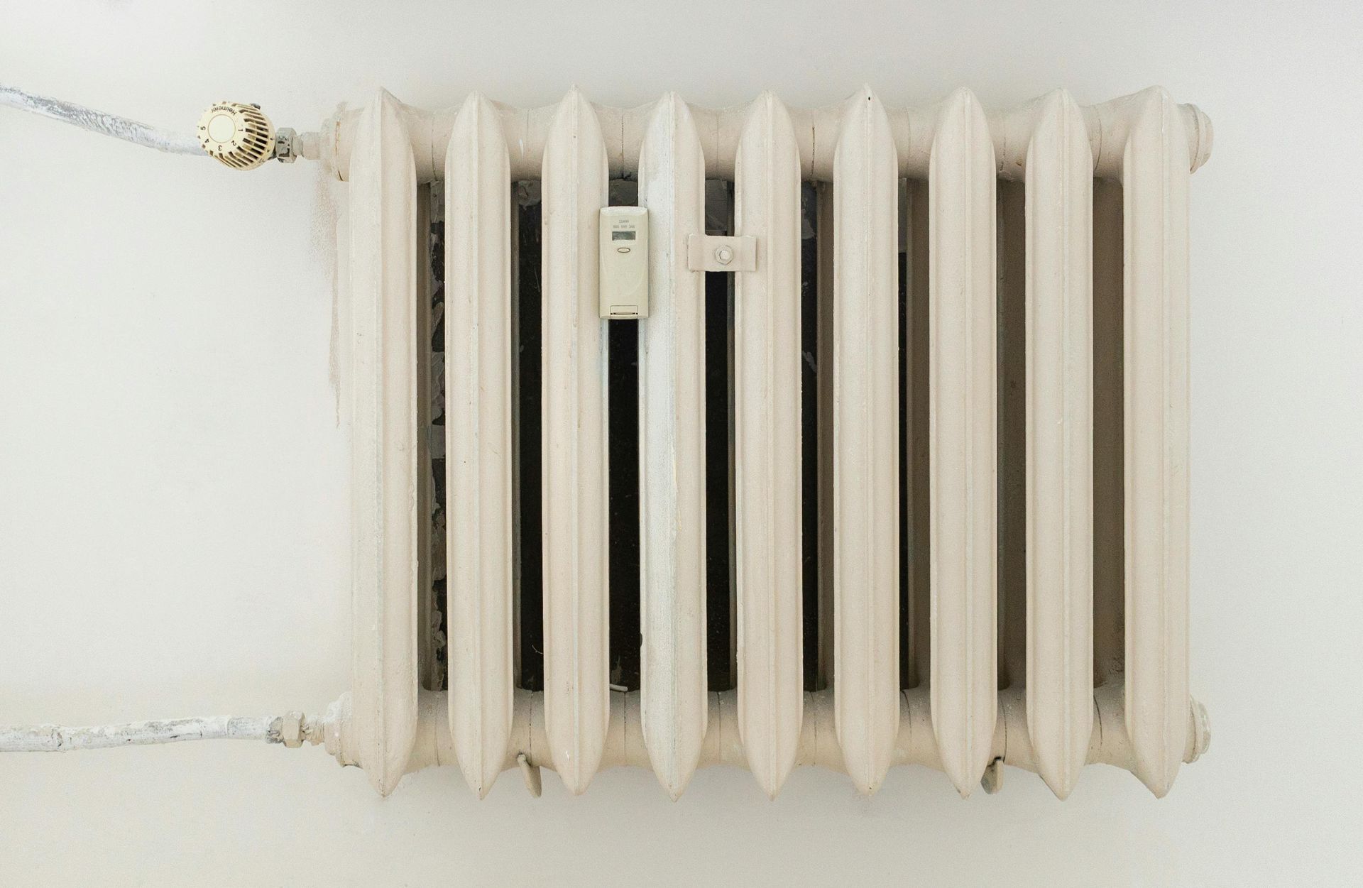 White cast-iron radiator with a small thermostat against a plain white wall