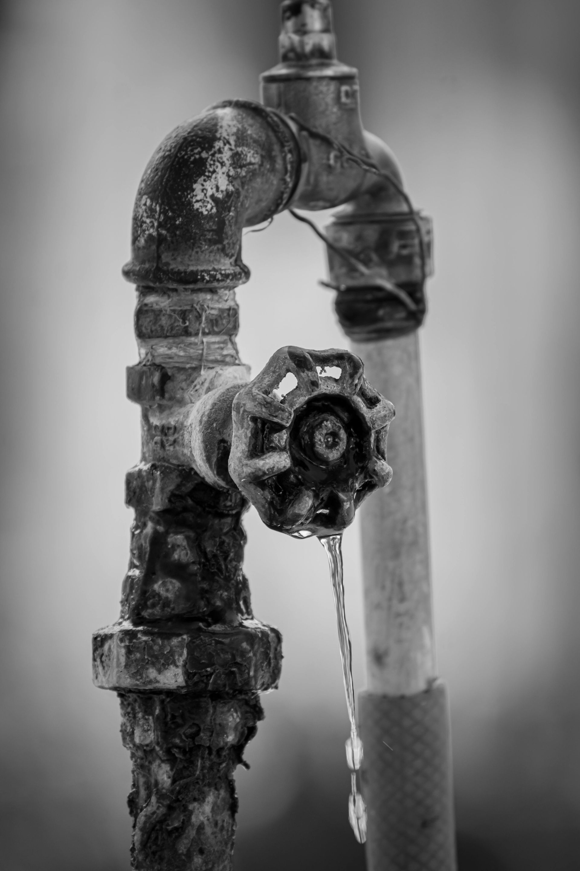 Old metal water spigot dripping in black and white.