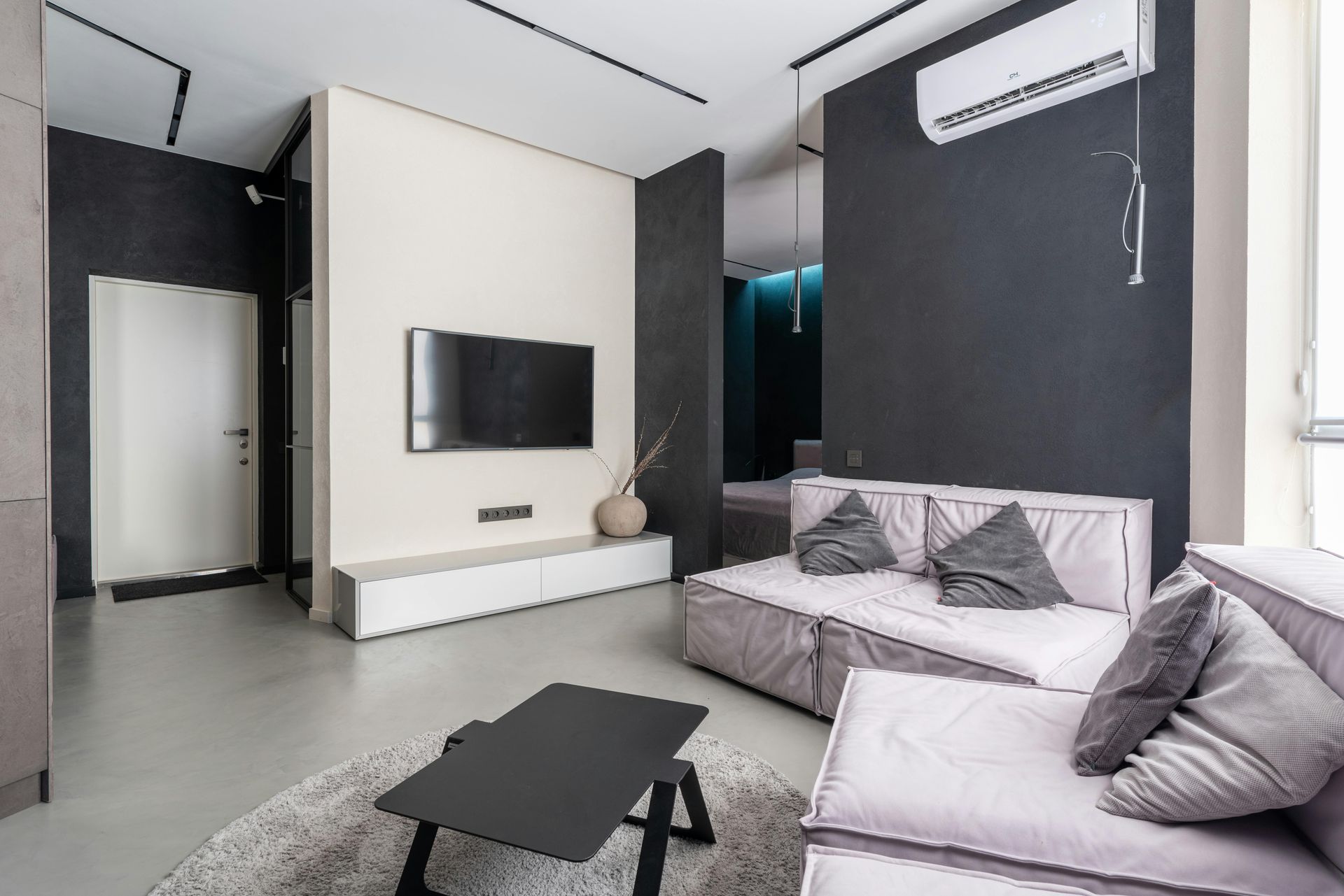 Modern living room with white sofa, wall-mounted TV, black accent walls, and air conditioner