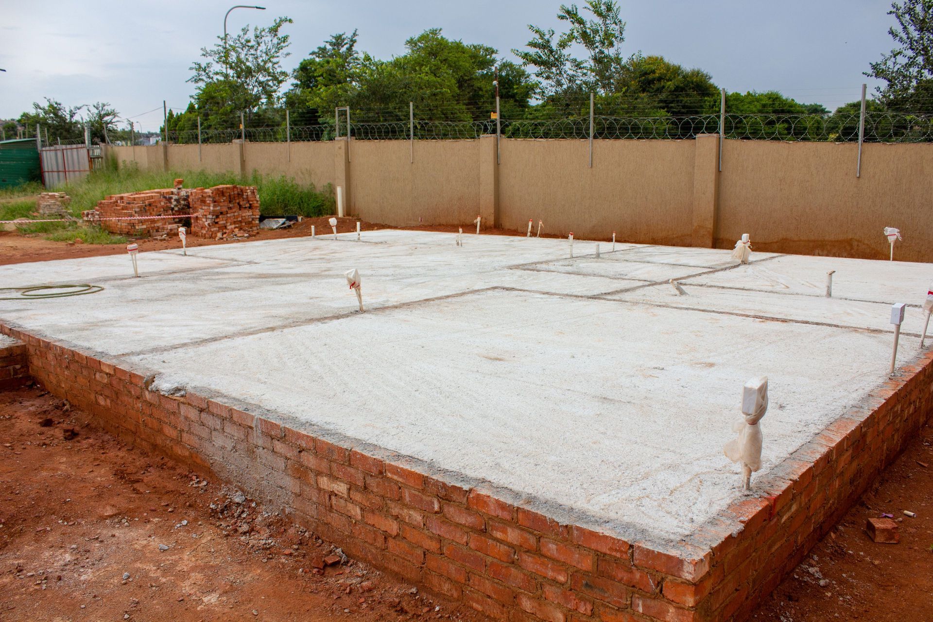 Newly poured concrete foundation with red brick walls, piping, and exposed dirt.