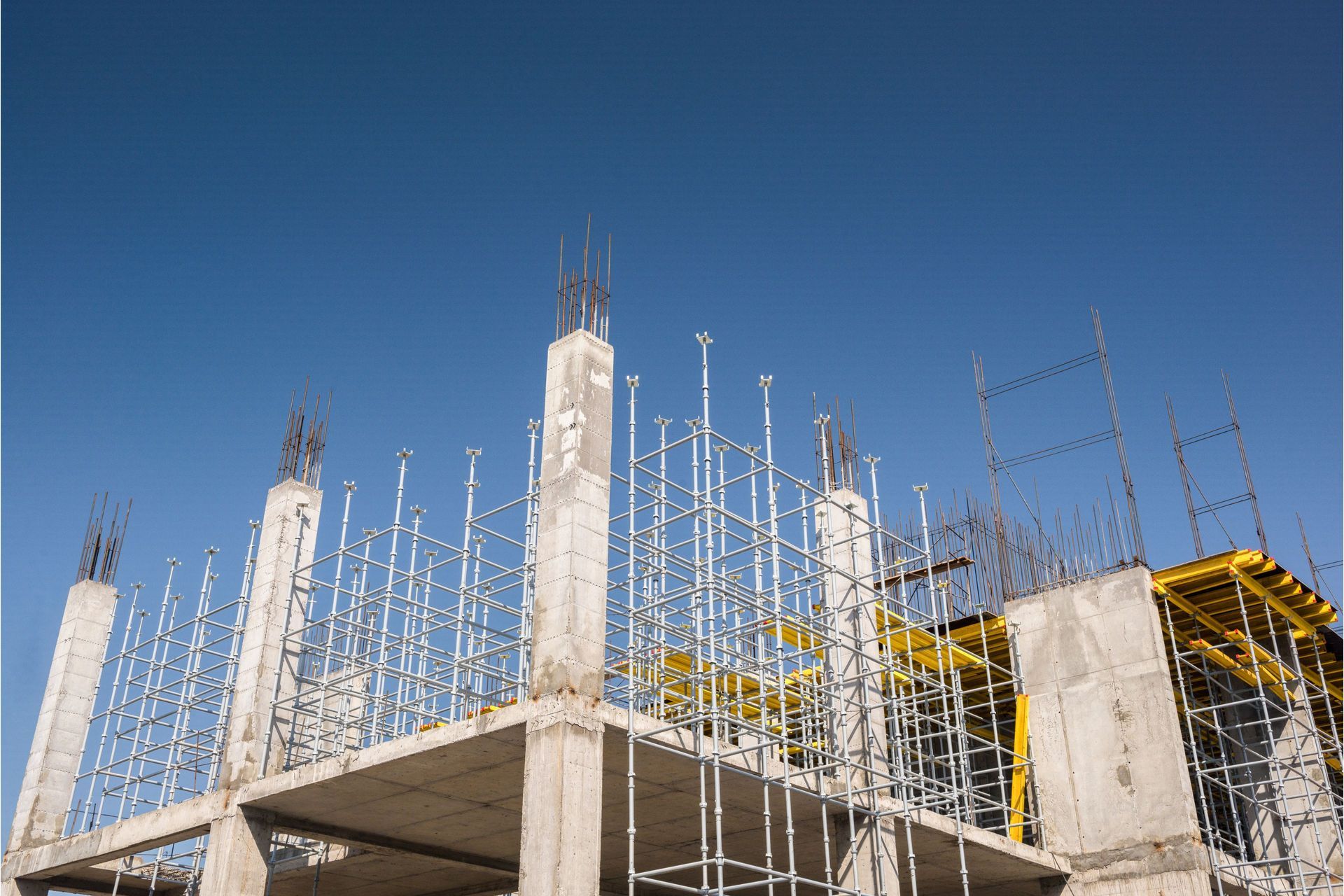 Concrete building frame under construction against a clear blue sky.