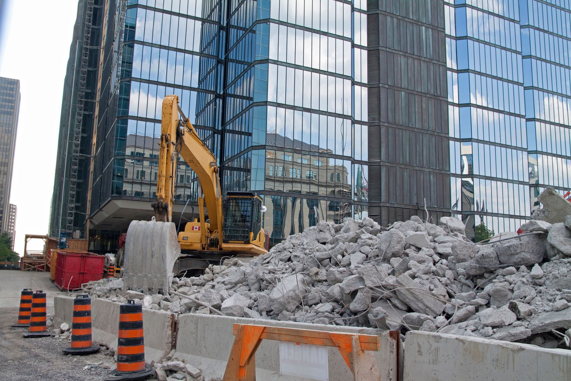 Yellow excavator moving debris near a tall, glass-faced building under construction.