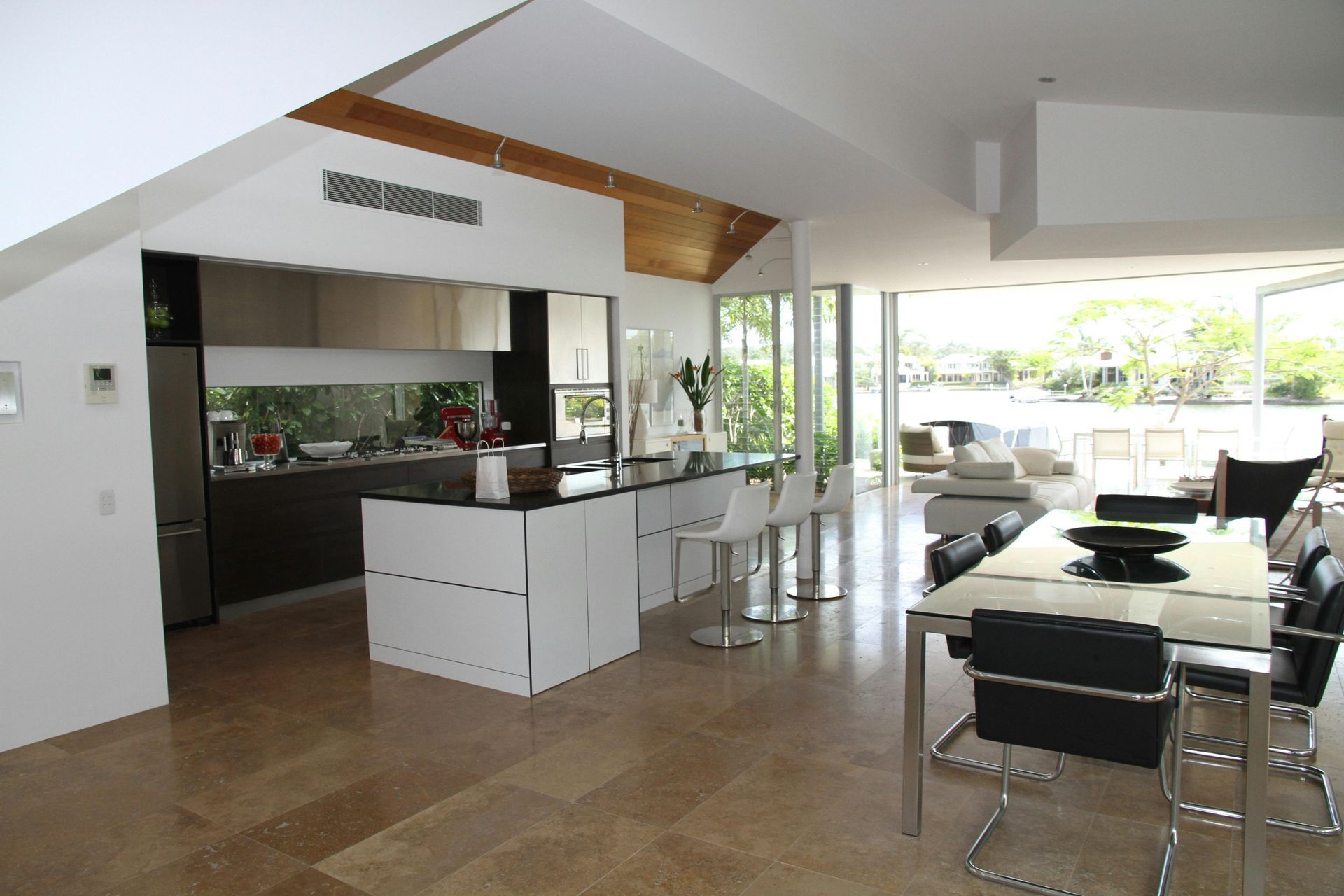 Modern open-plan kitchen and dining area with island, bar stools, and table; overlooking waterfront.