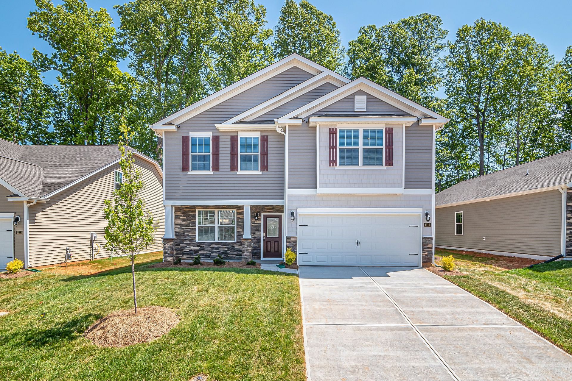Two-story gray house with red shutters and a driveway; green lawn and trees in the background.