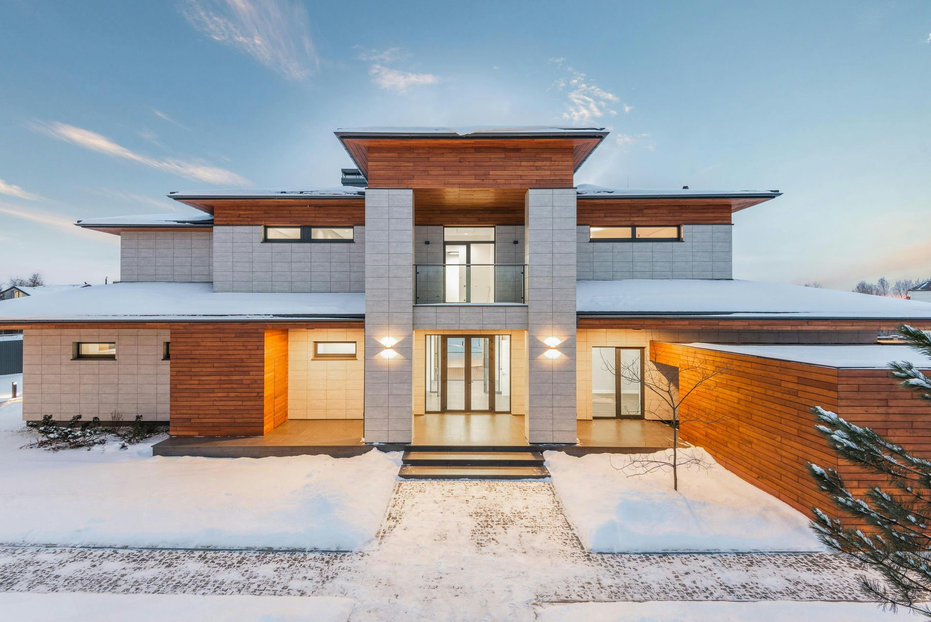 Modern two-story house with light stone and wood accents, snow-covered ground.