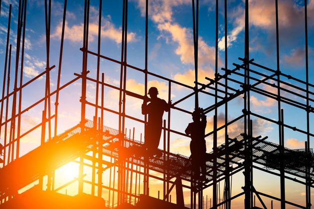 Construction workers on scaffolding at sunset.