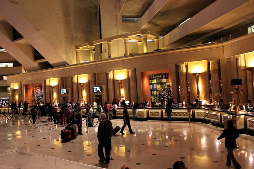 Lobby with people at a hotel check-in counter. Soft lighting, reflective floor, various people and luggage present.