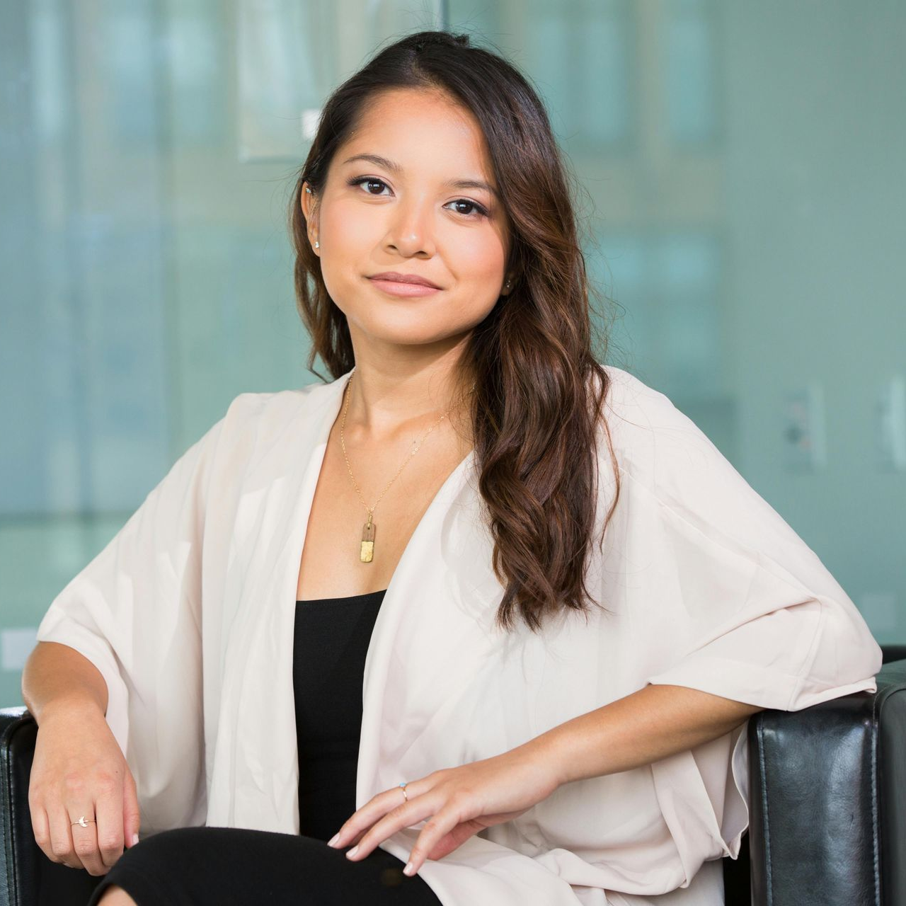Woman with brown hair in beige wrap and black top, sitting in black chair.
