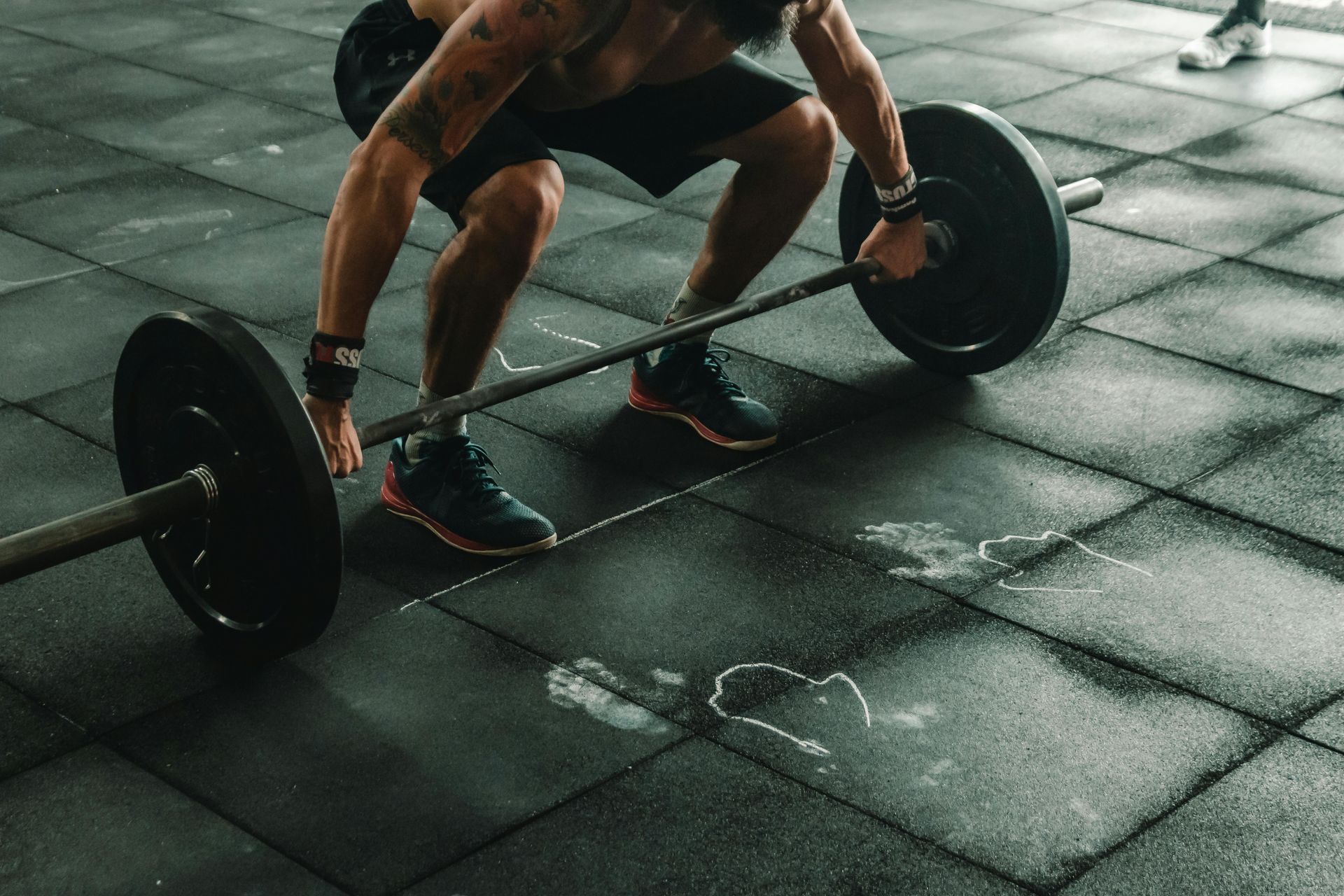Man lifting barbell in gym. Black weights, dark floor.