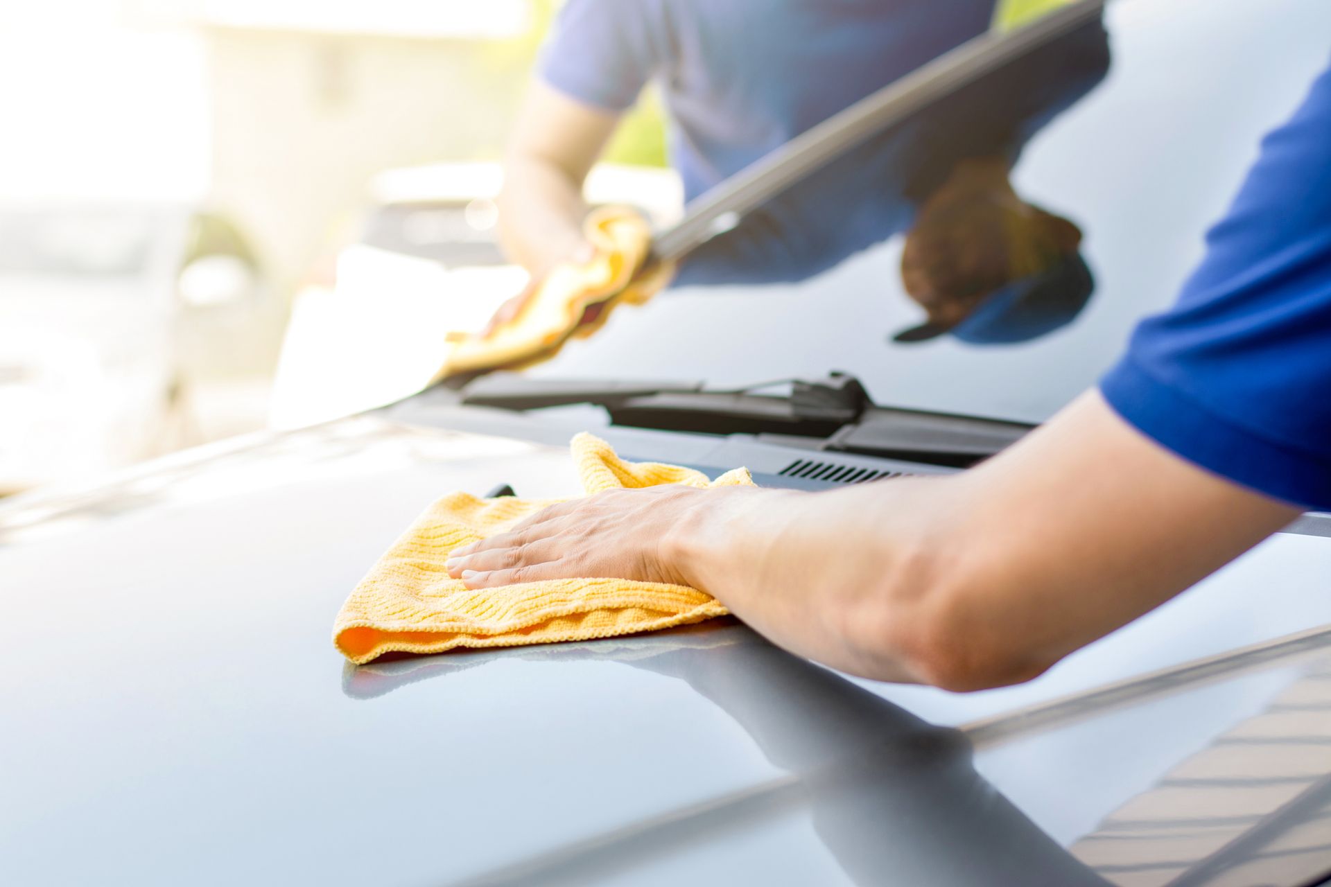 Person cleaning a car windshield with a yellow cloth and squeegee