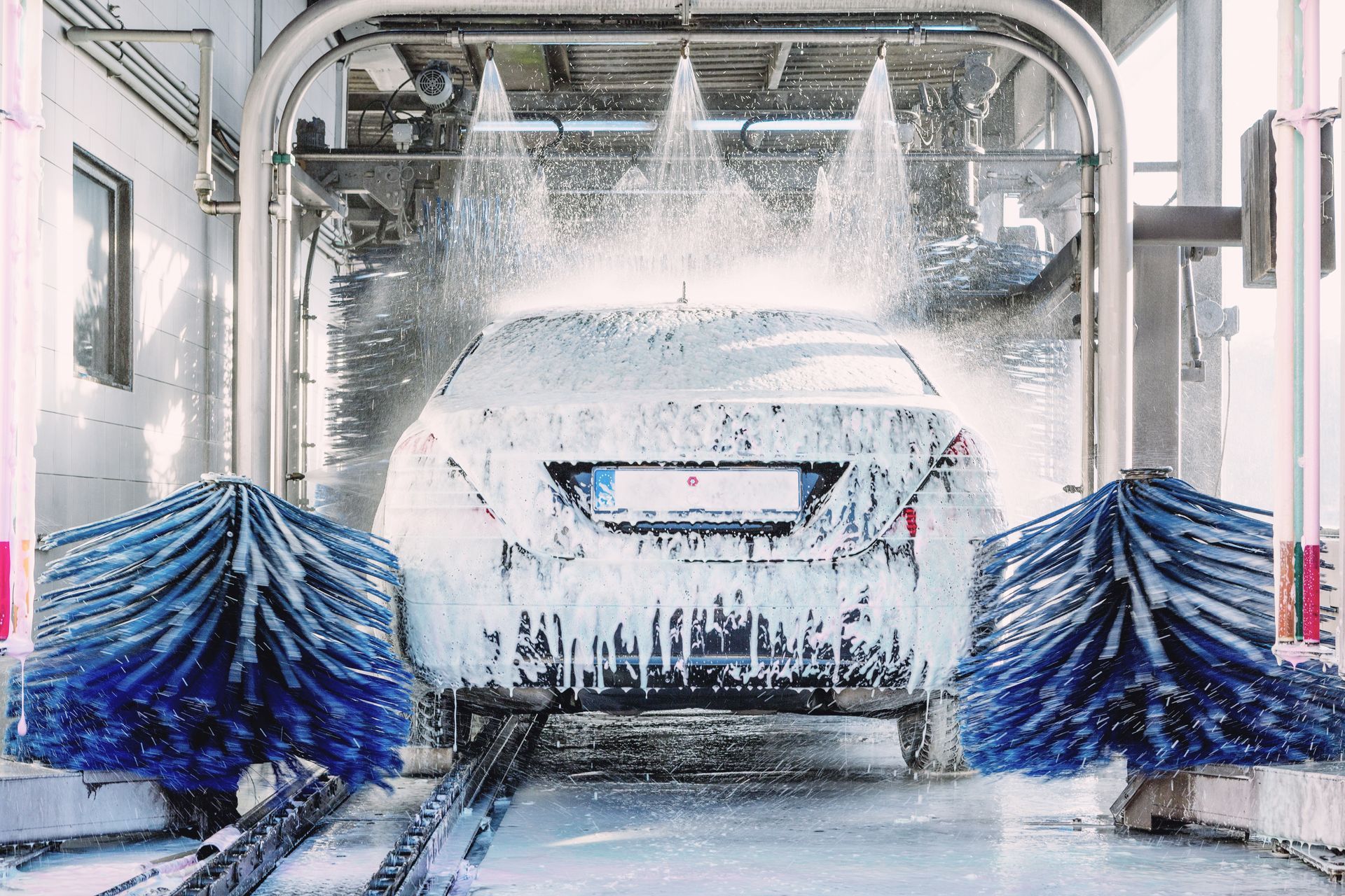 Car wash tunnel with blue brushes spraying water over a vehicle