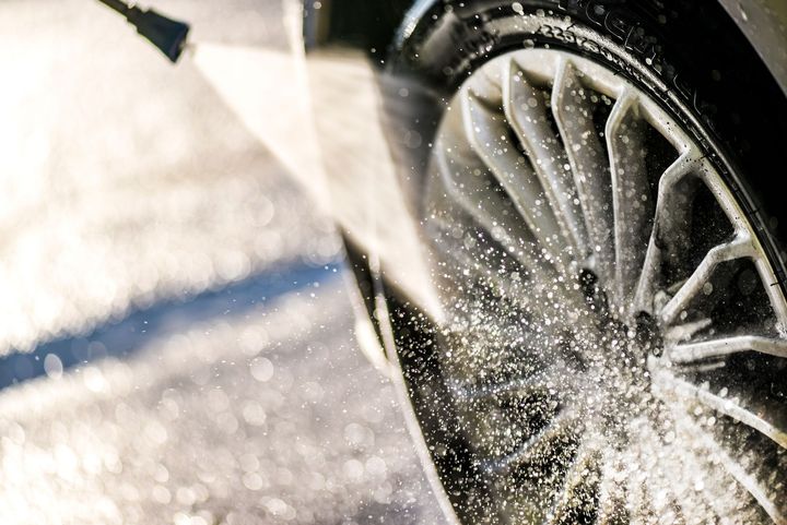 Close-up of a car wheel spraying water during a wash, with sunlight glinting off the wet tire.