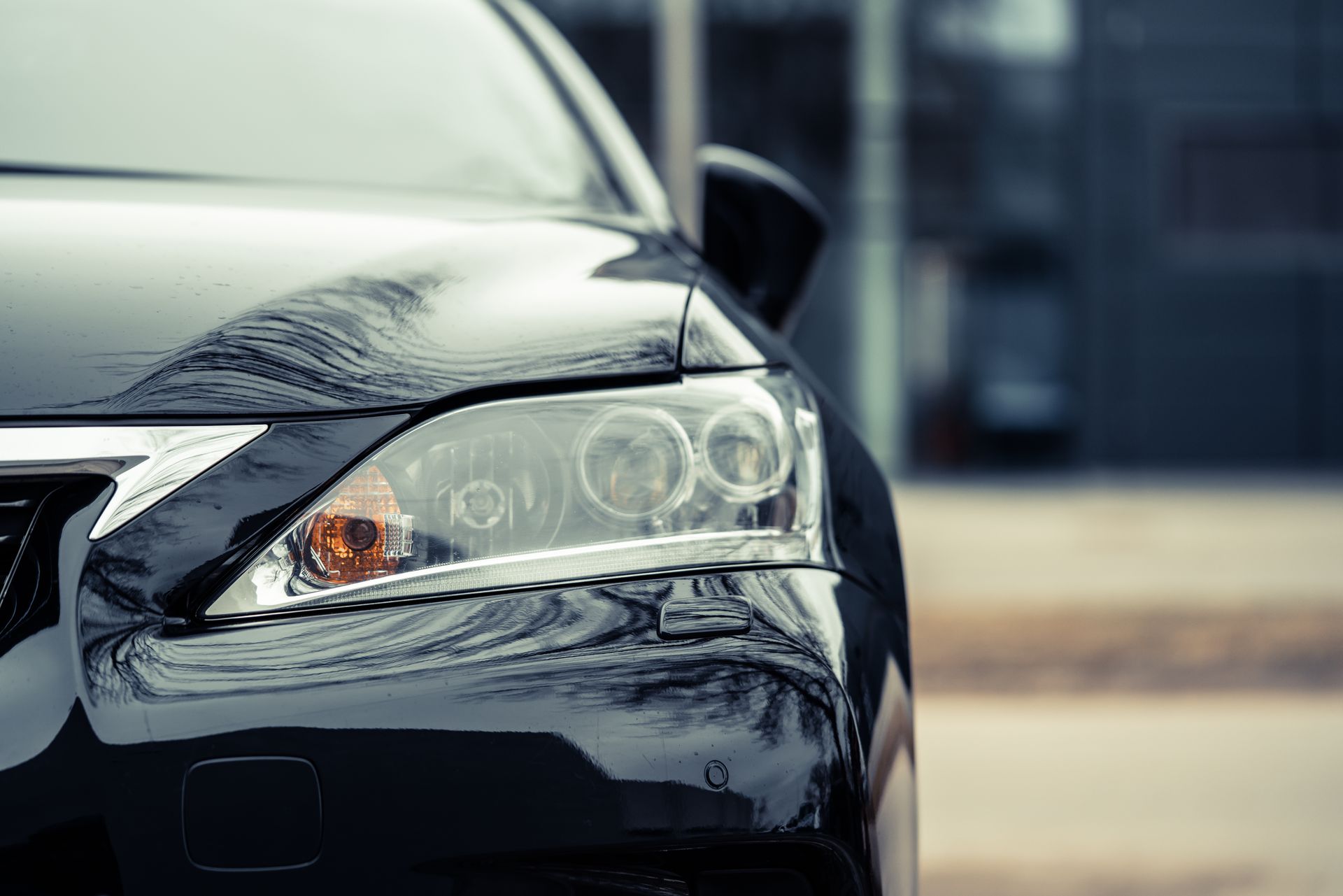 Close-up of a black car’s front headlight and hood in a parking area